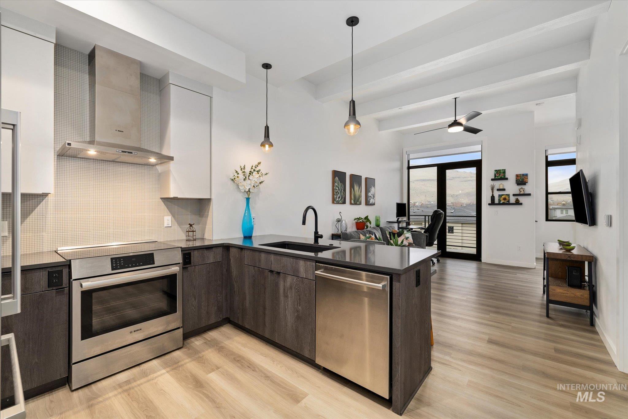 Kitchen featuring a peninsula, backsplash, wall chimney exhaust hood, stainless steel appliances, and open floor plan