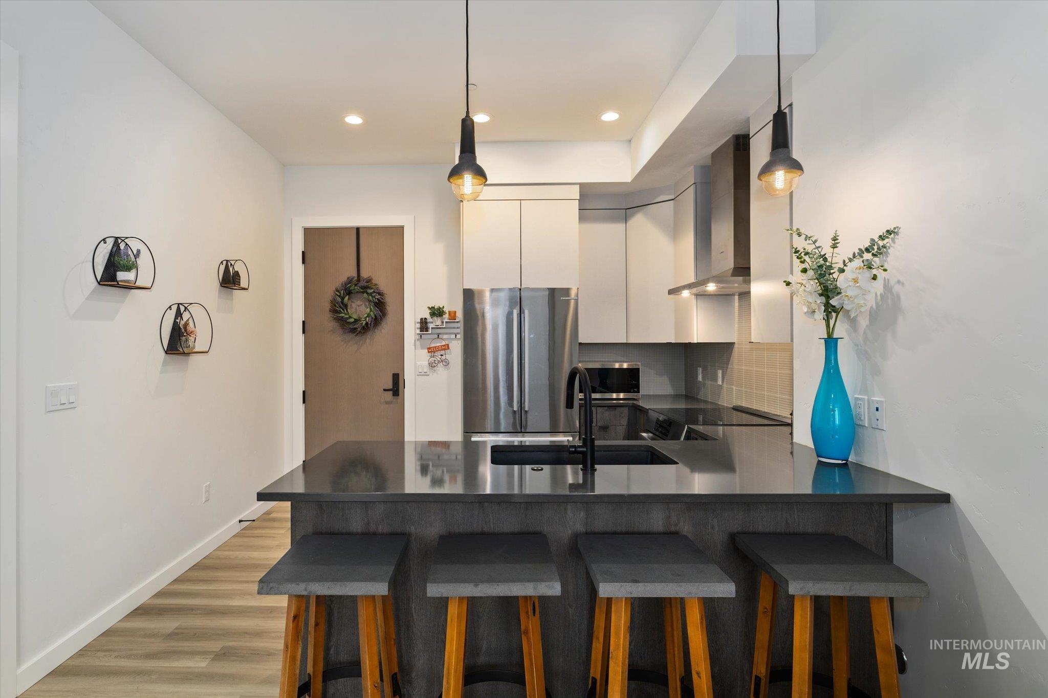 Kitchen with a kitchen bar, decorative backsplash, stainless steel appliances, hanging light fixtures, and wall chimney exhaust hood