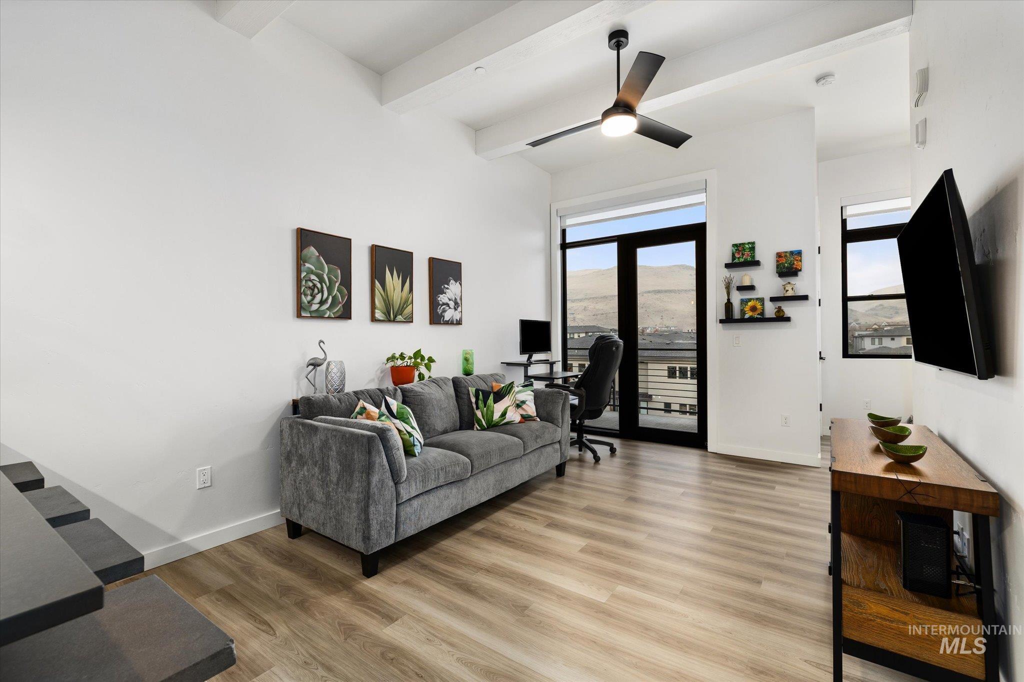 Living room with an office area, beam ceiling, light wood finished floors, and a ceiling fan