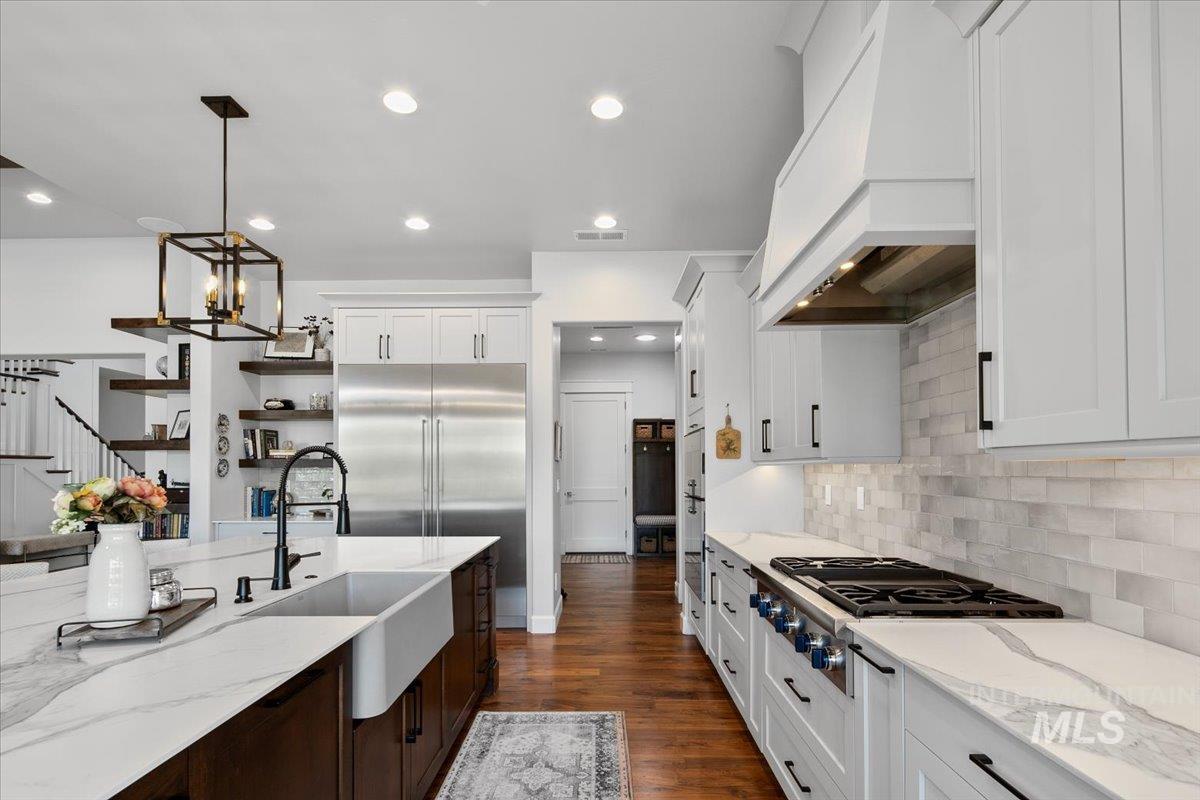 Kitchen featuring dark wood finished floors, appliances with stainless steel finishes, white cabinetry, decorative light fixtures, and light stone countertops