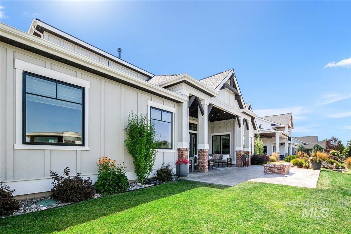 Back of house with board and batten siding, a patio area, a lawn, and a shingled roof