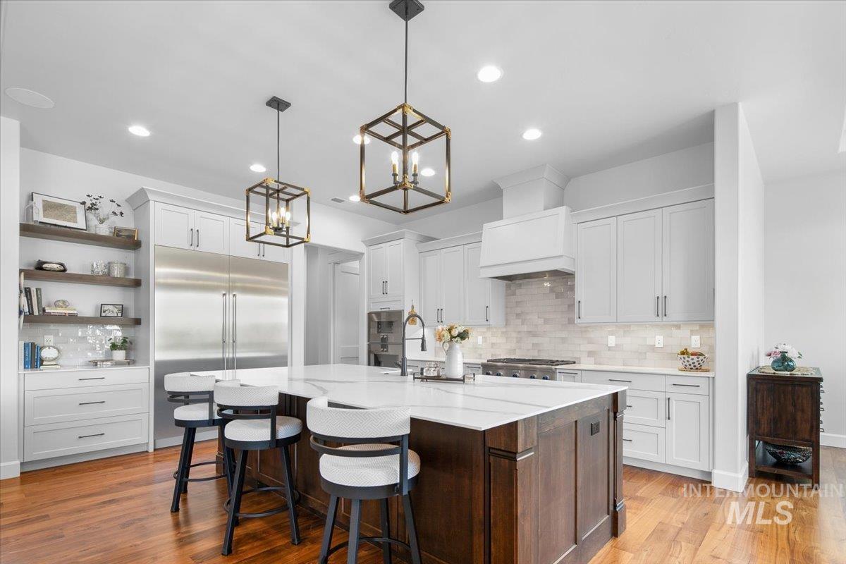 Kitchen featuring backsplash, light wood-style floors, stainless steel appliances, a chandelier, and a kitchen island with sink