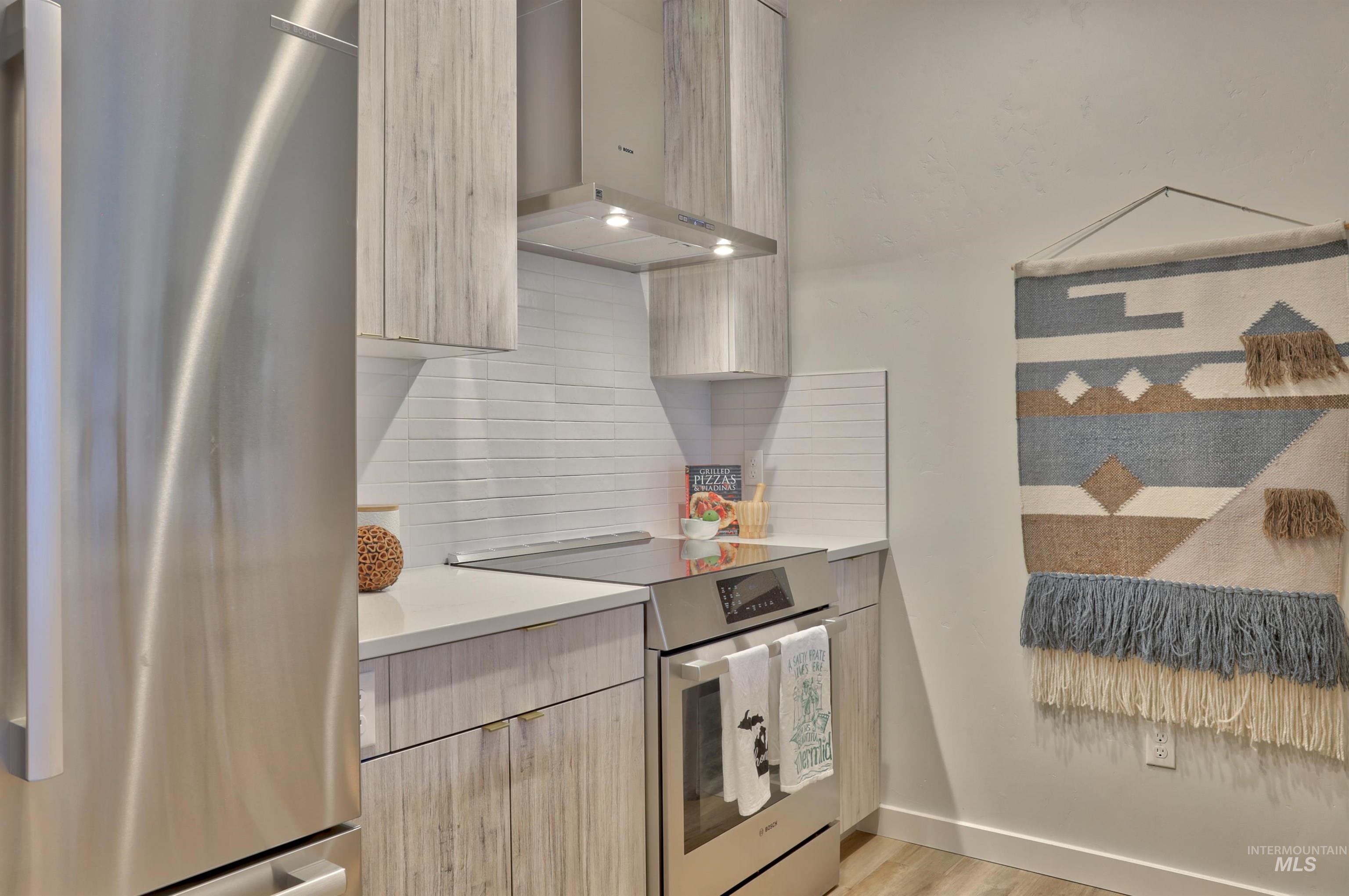 Kitchen featuring appliances with stainless steel finishes, exhaust hood, light brown cabinets, modern cabinets, and backsplash