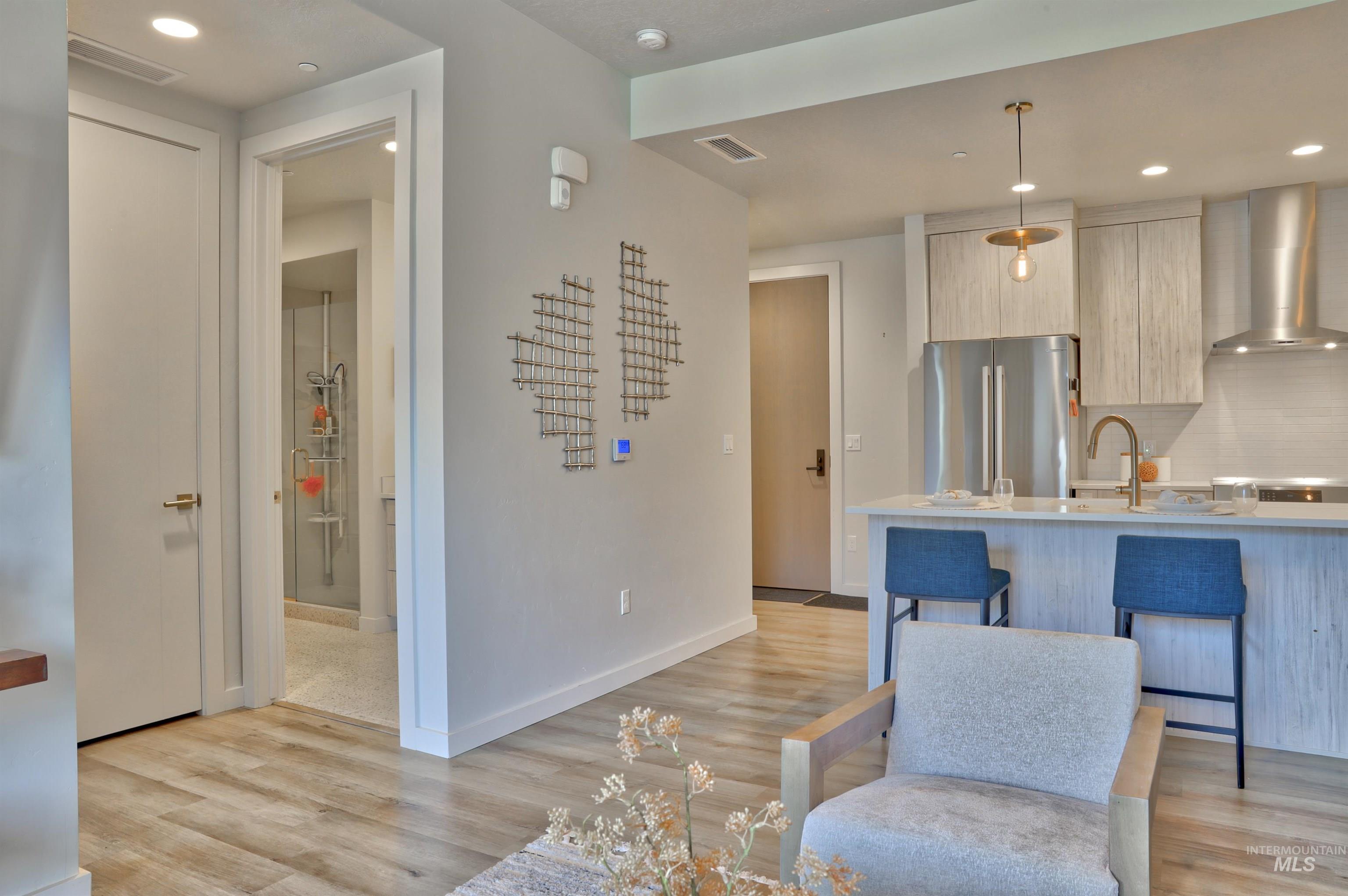 Kitchen featuring recessed lighting, wall chimney range hood, freestanding refrigerator, modern cabinets, and light wood-style floors