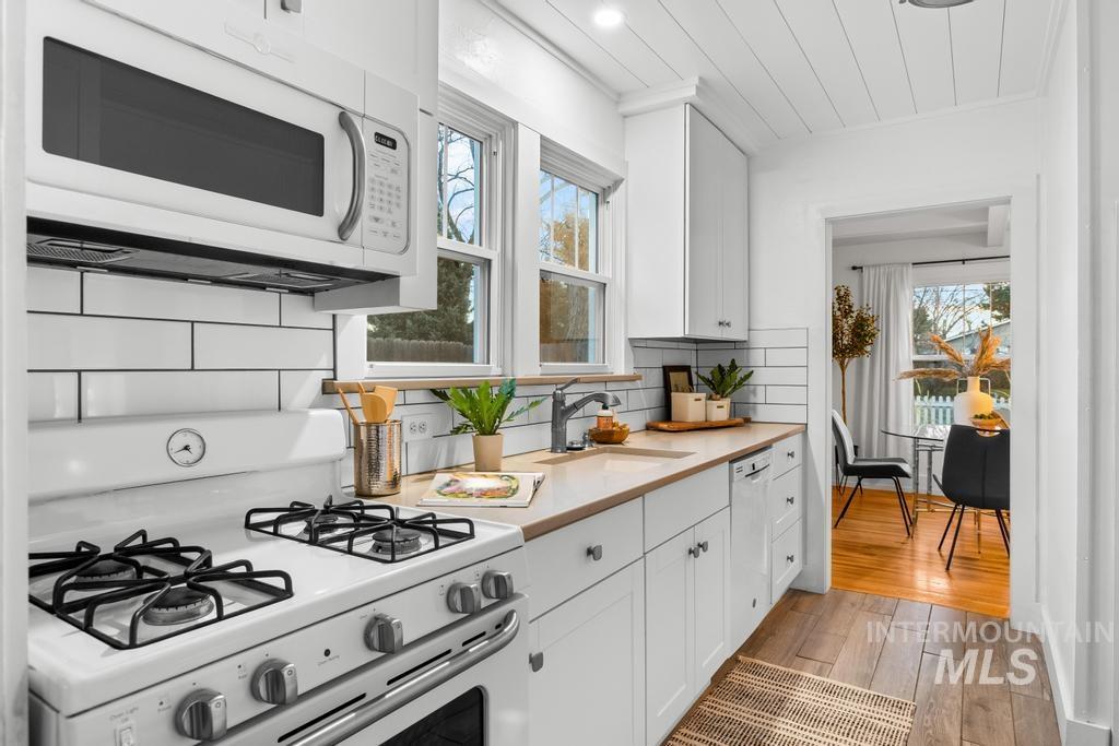 Kitchen with white appliances, white cabinetry, light countertops, dark wood-style flooring, and backsplash