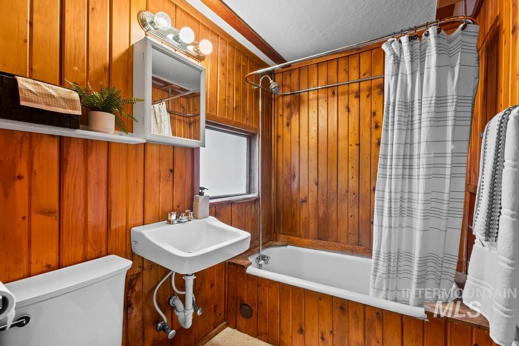 Bathroom featuring shower / tub combo and wood walls