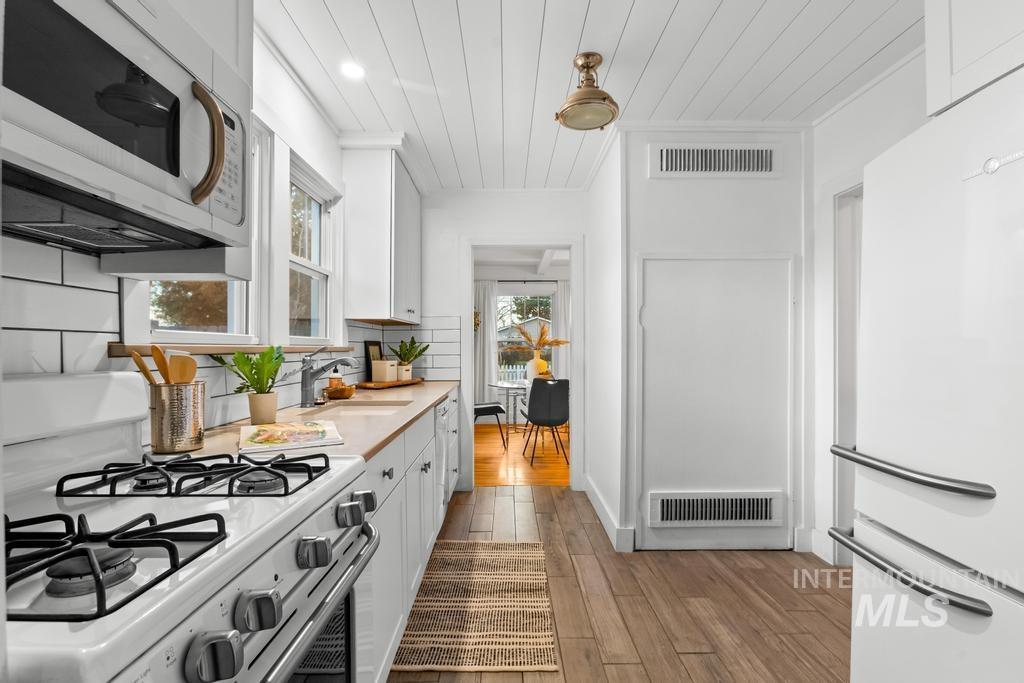 Kitchen with white appliances, wood ceiling, light countertops, dark wood-style flooring, and white cabinets