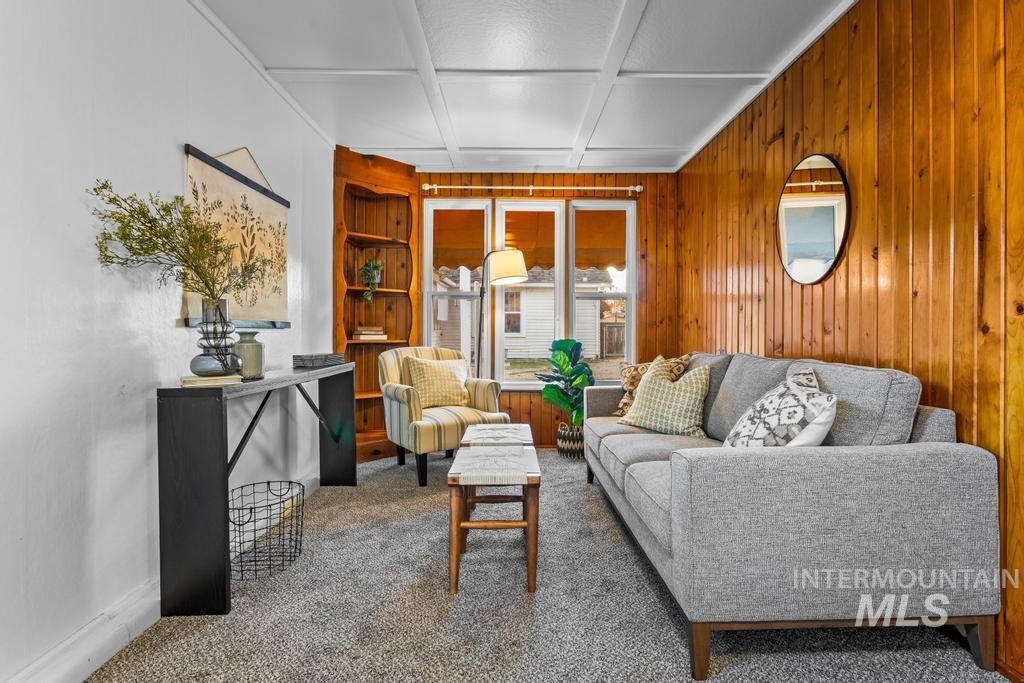 Carpeted living room featuring built in shelves, coffered ceiling, wooden walls, and beam ceiling