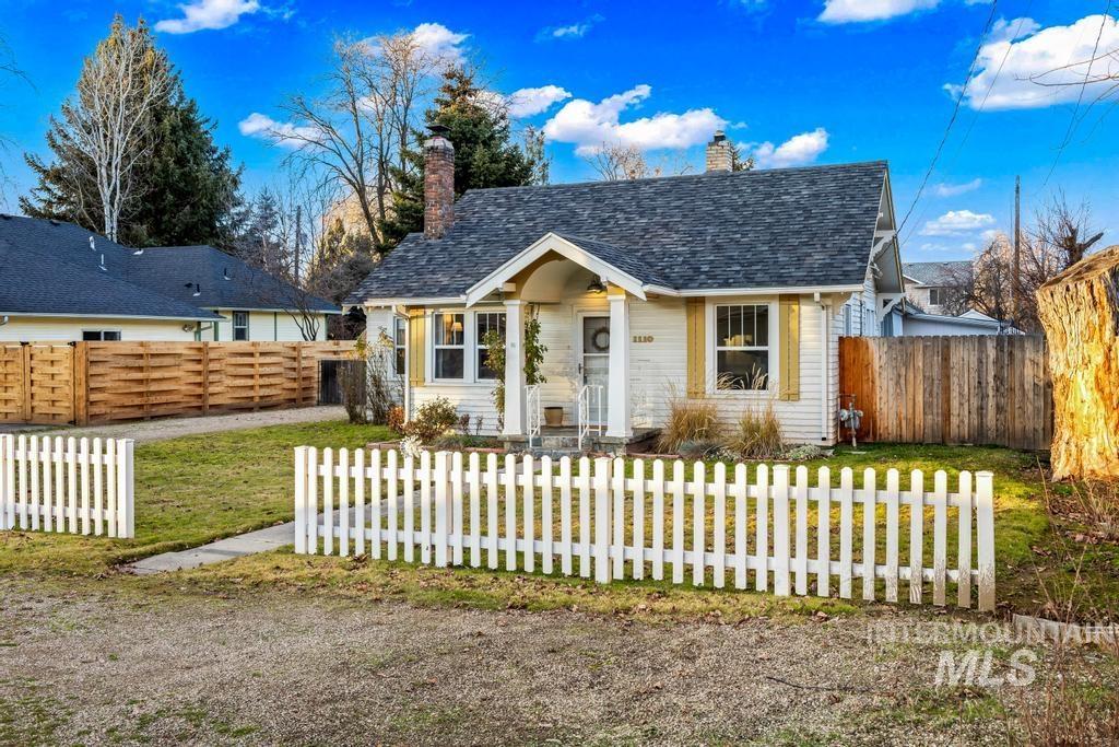 Bungalow-style house with a chimney, a fenced front yard, and a shingled roof