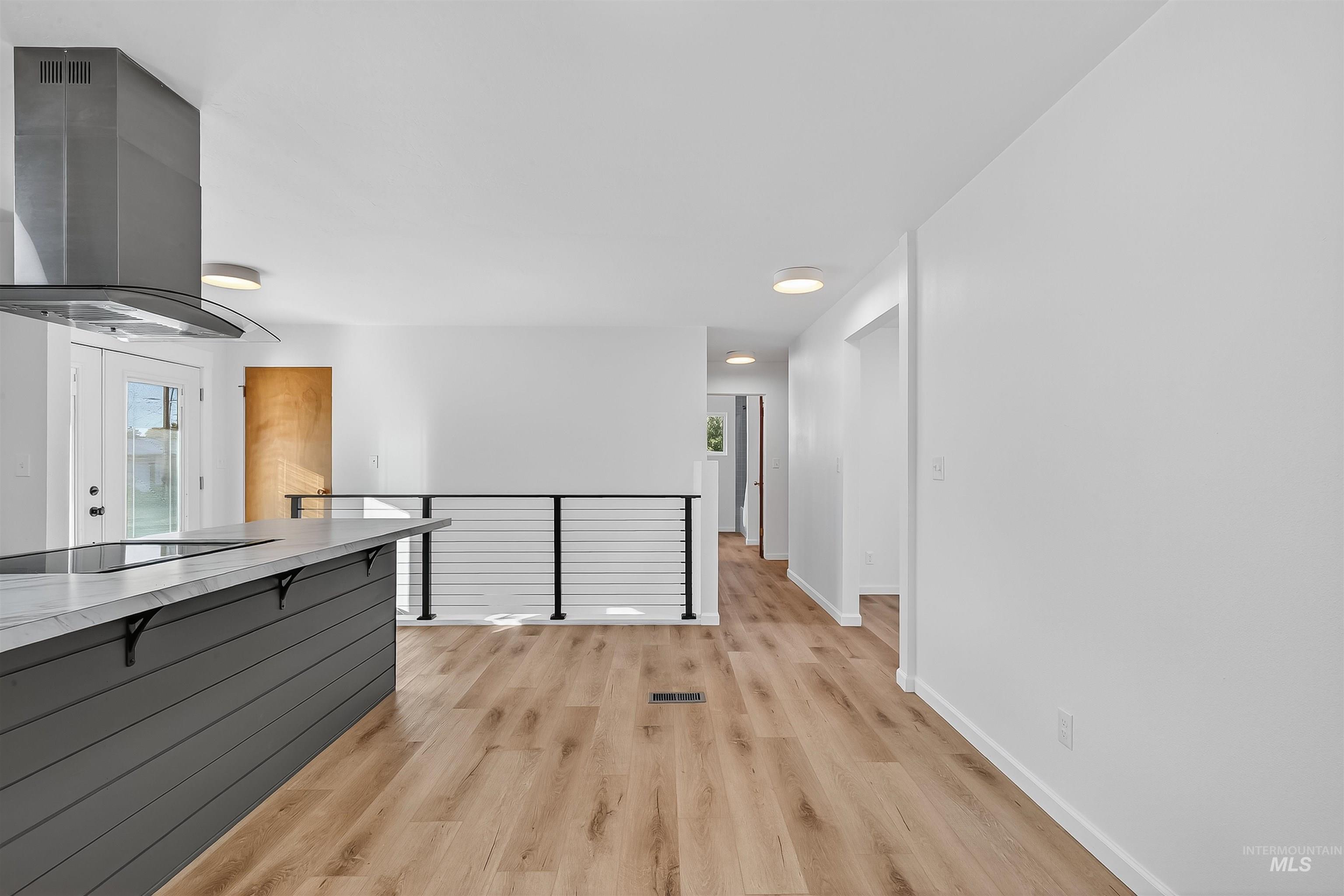 Kitchen featuring exhaust hood, a kitchen breakfast bar, light wood-type flooring, light countertops, and black electric cooktop