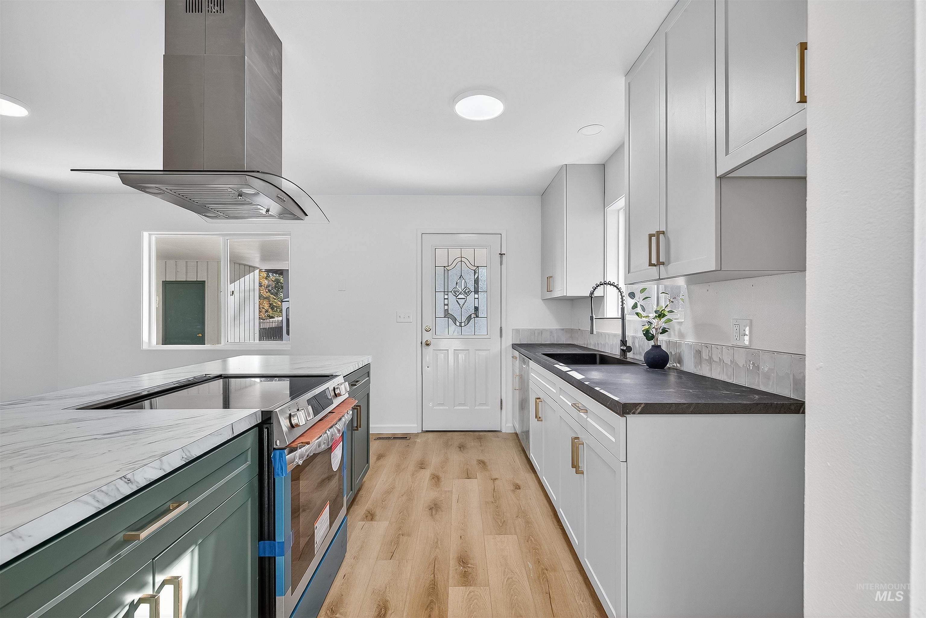 Kitchen with stainless steel appliances, island exhaust hood, light wood-type flooring, white cabinetry, and dark countertops