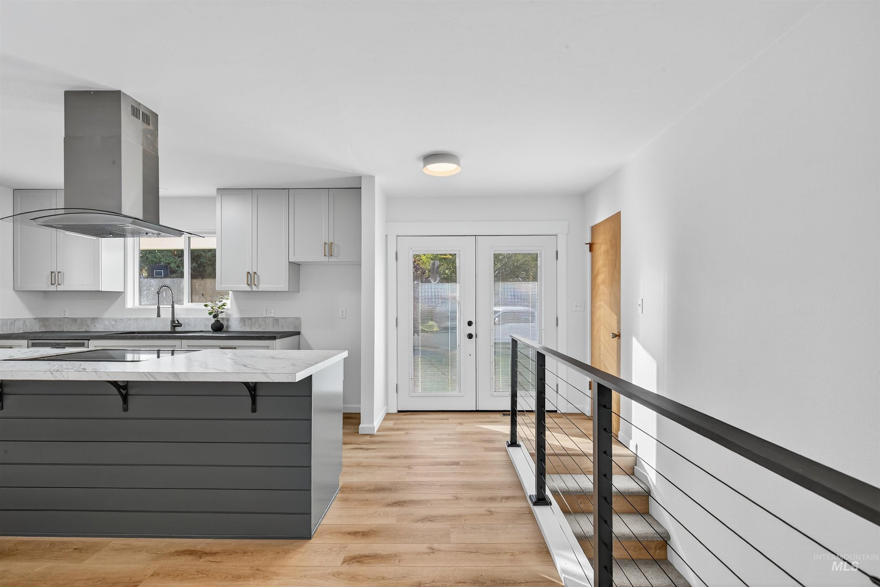 Kitchen with french doors, white cabinetry, light wood-type flooring, island range hood, and a breakfast bar area