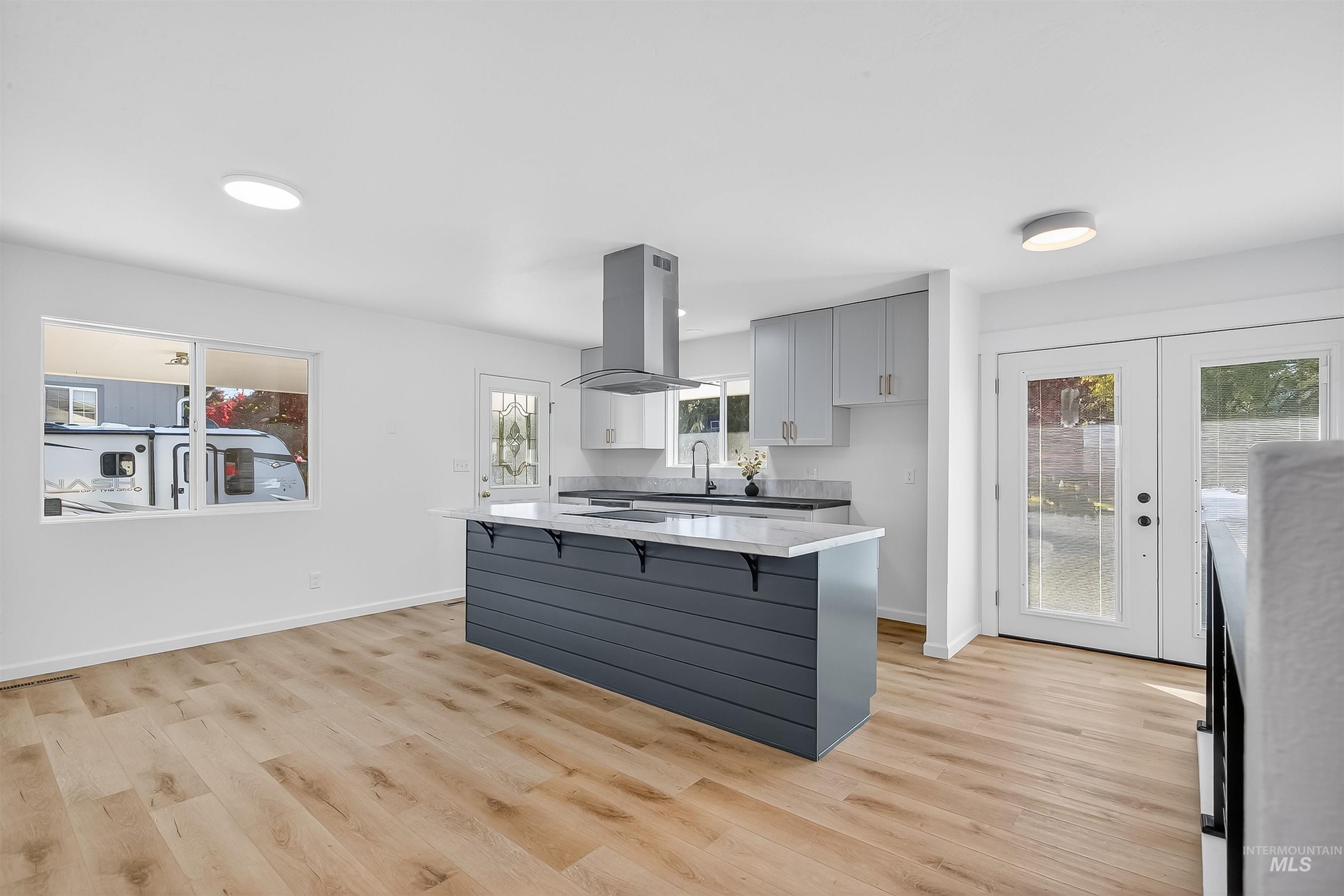 Kitchen with gray cabinetry, a kitchen breakfast bar, light wood-style floors, and a center island