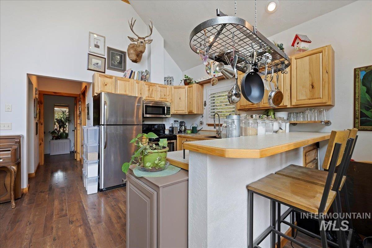 Kitchen featuring appliances with stainless steel finishes, light countertops, a kitchen breakfast bar, dark wood-style floors, and high vaulted ceiling