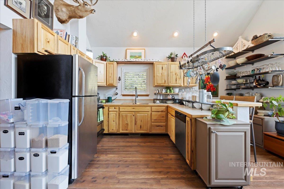 Kitchen with dark wood-style floors, light brown cabinetry, appliances with stainless steel finishes, a peninsula, and lofted ceiling