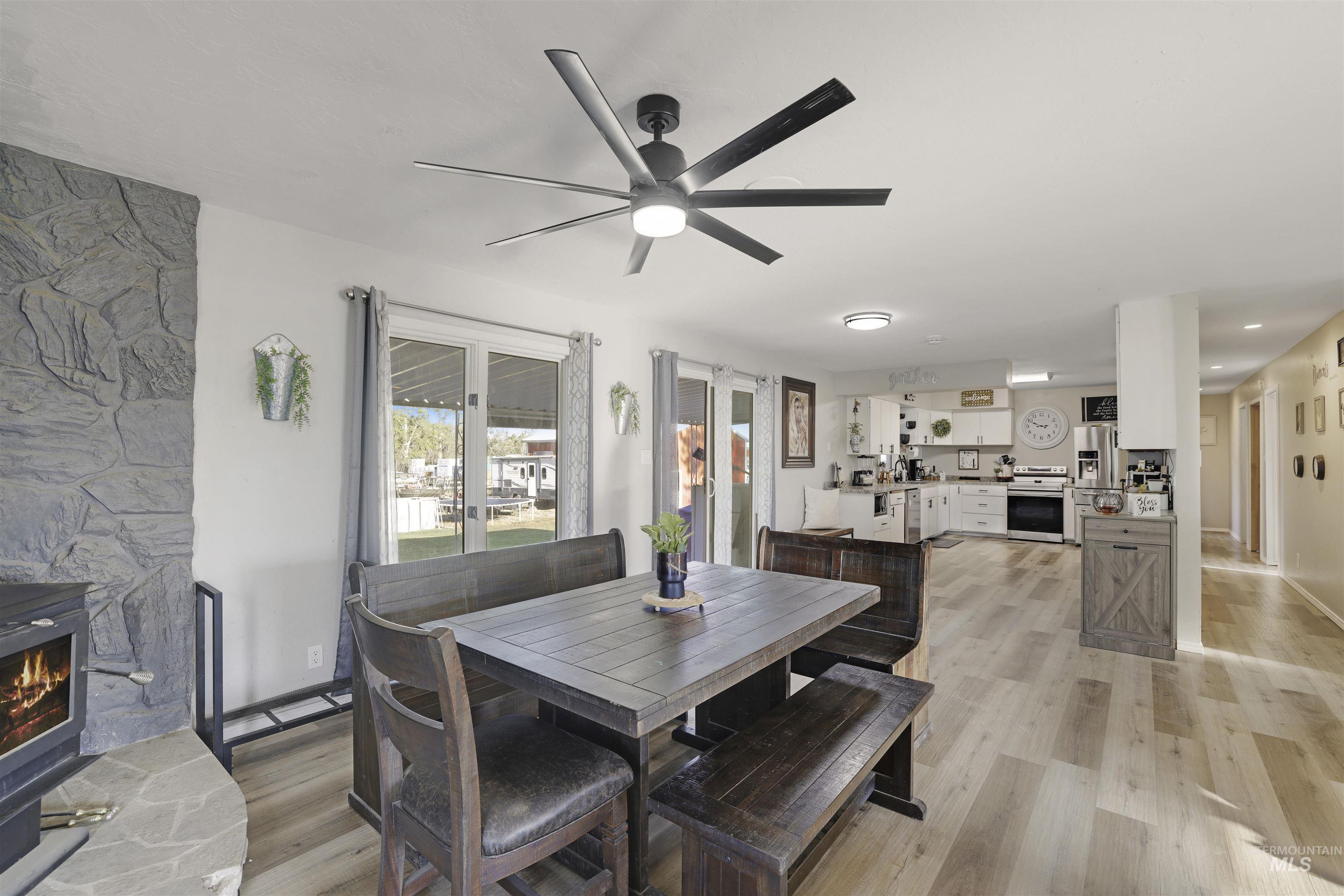 Dining space with light wood-style floors, ceiling fan, and a wood stove