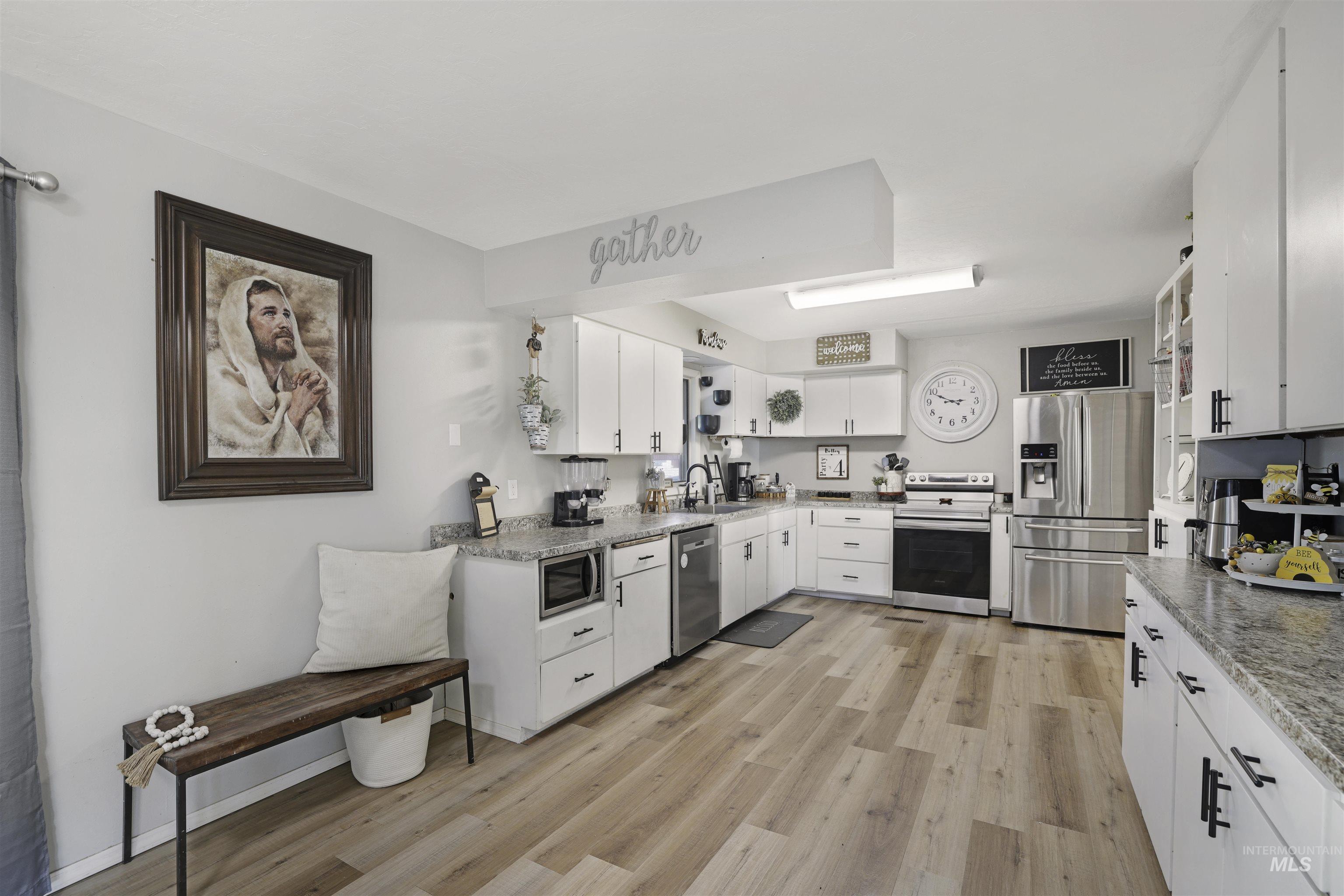 Kitchen with stainless steel appliances, white cabinets, light wood-style flooring, and light stone counters