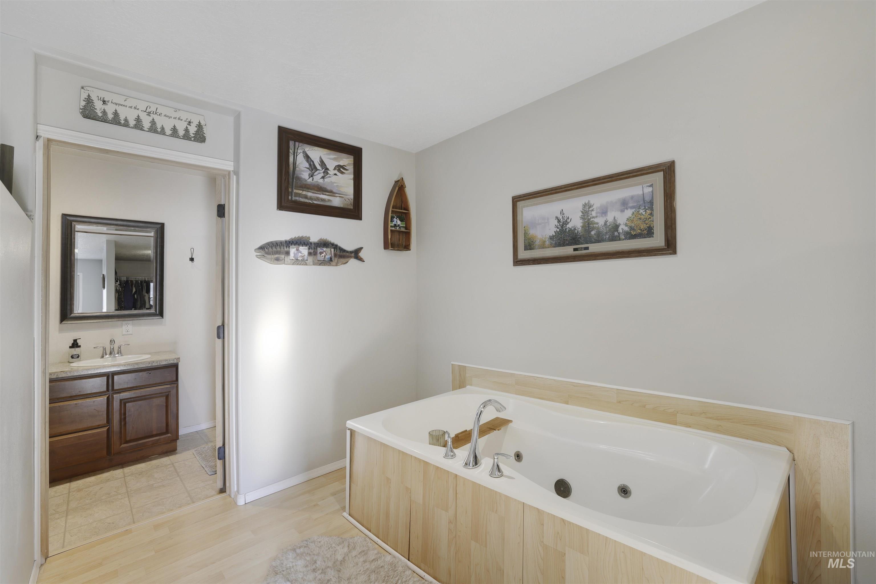 Full bath featuring a whirlpool tub, vanity, and light wood-style flooring