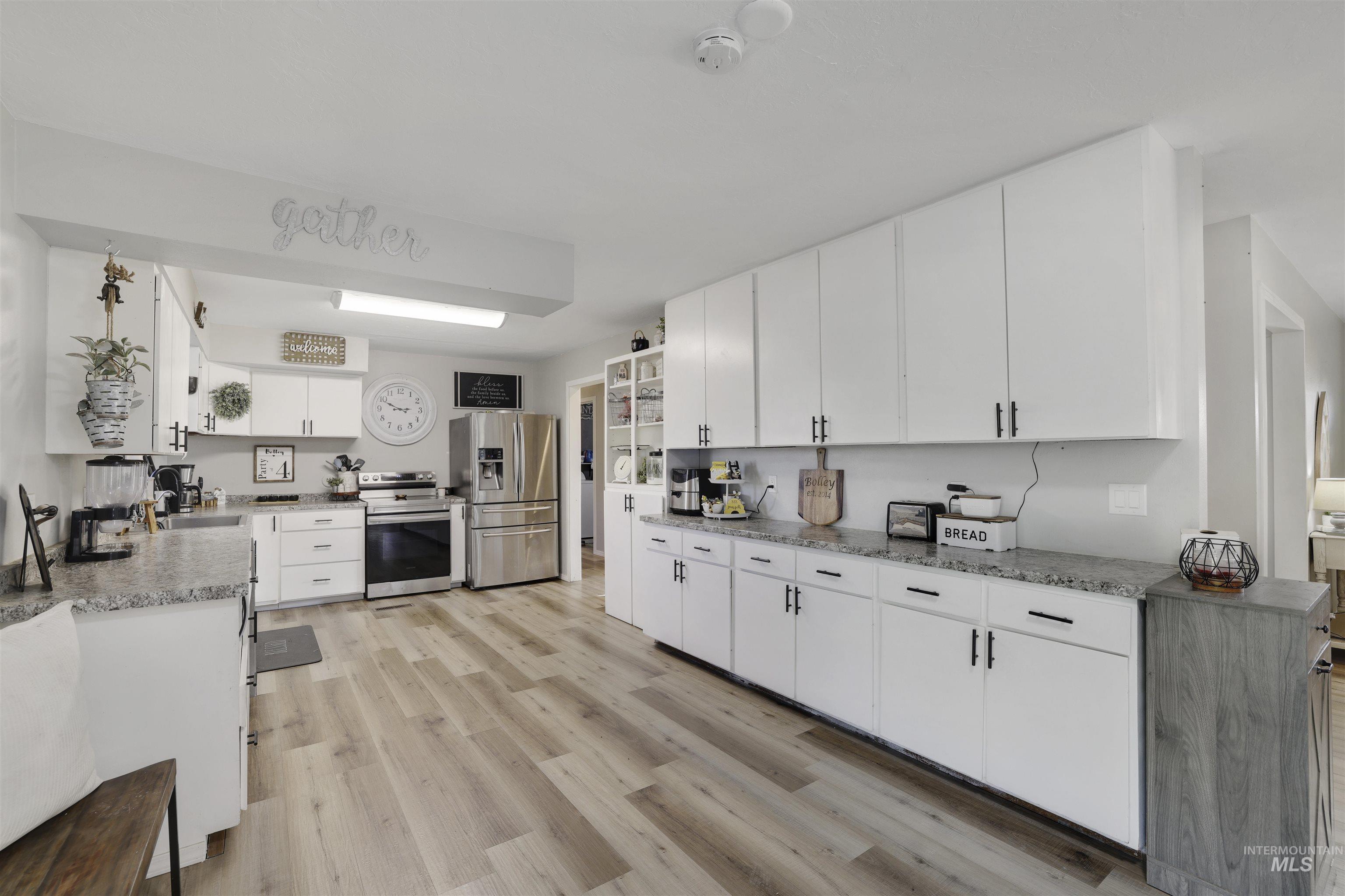 Kitchen featuring white cabinetry, stainless steel appliances, light wood-style floors, and light stone counters