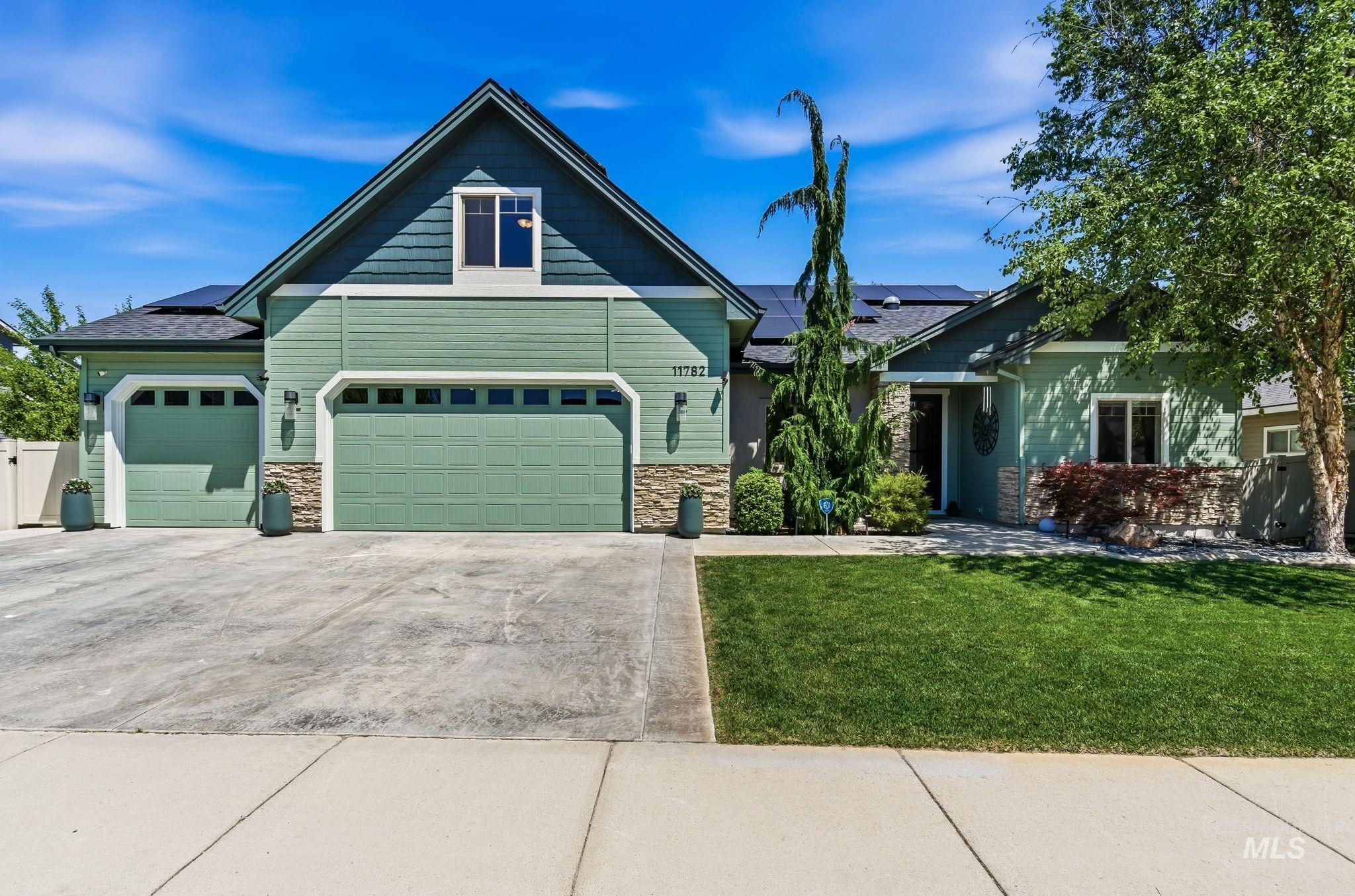 Traditional-style residence featuring a multi-tone green exterior with stone accents, a two-car garage, an additional single-car garage, and a concrete driveway