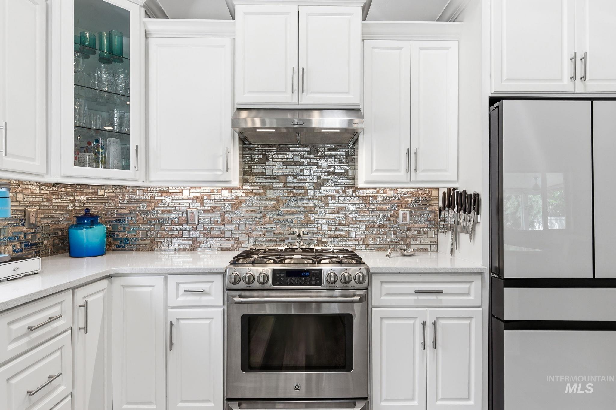 Modern kitchen featuring white cabinetry with brushed nickel hardware, a stainless steel range with overhead hood, and a reflective tile backsplash