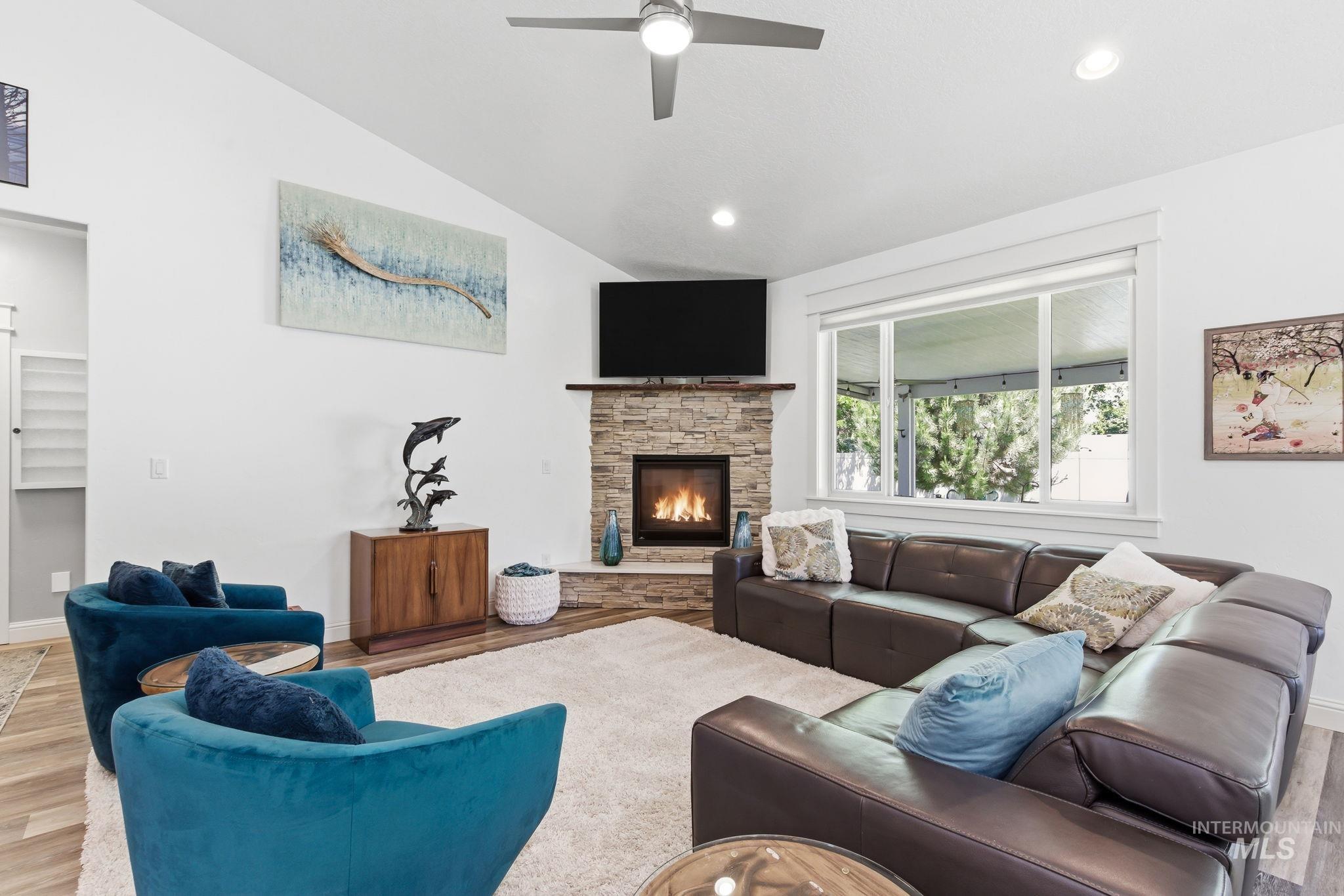 Vaulted ceiling living room featuring a corner stone fireplace, wood-finish flooring, recessed lighting, and a ceiling fan