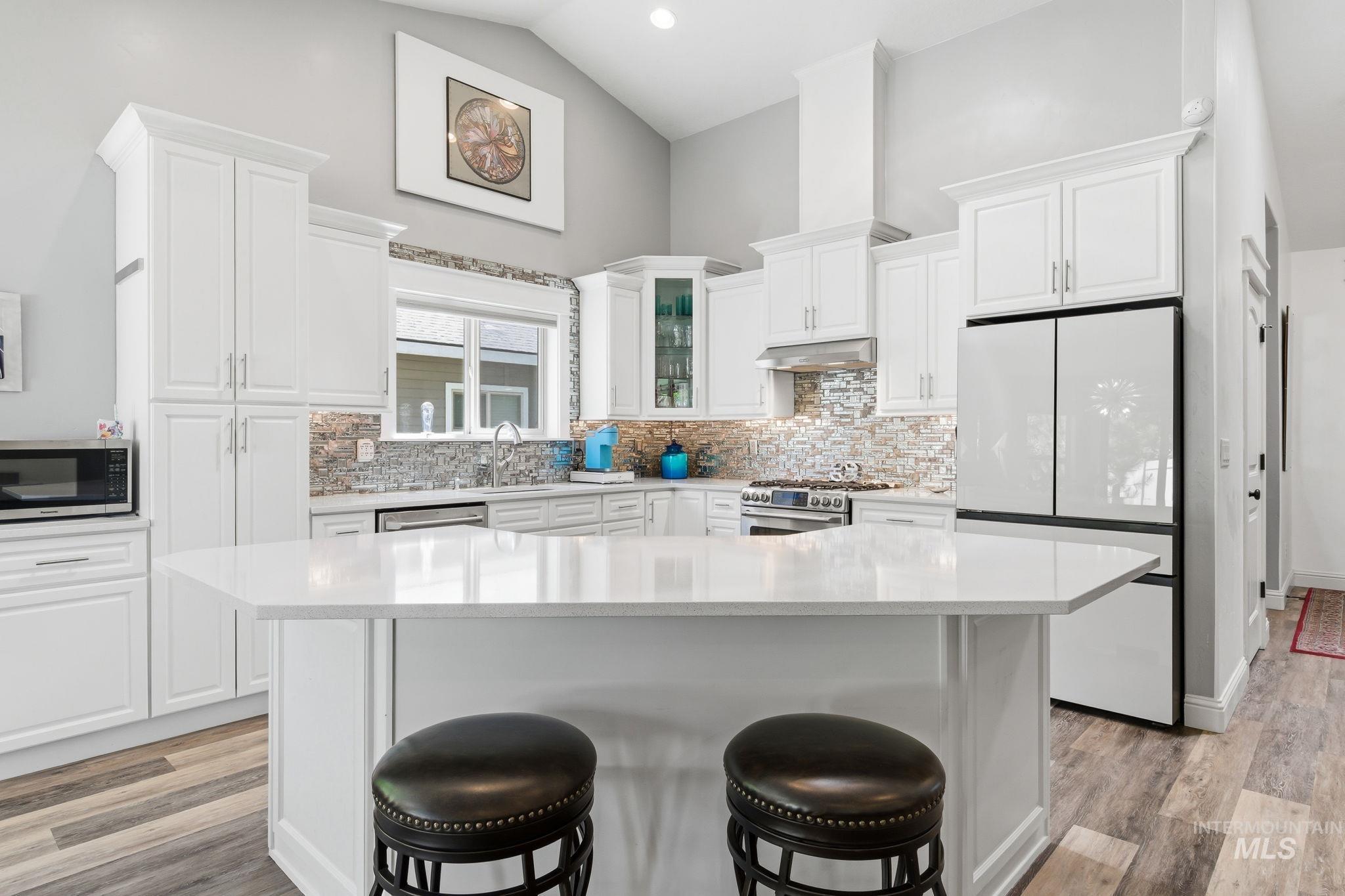 Kitchen featuring a central island with a light-toned countertop, white cabinetry, a decorative tile backsplash, stainless steel appliances, and wood-finish flooring