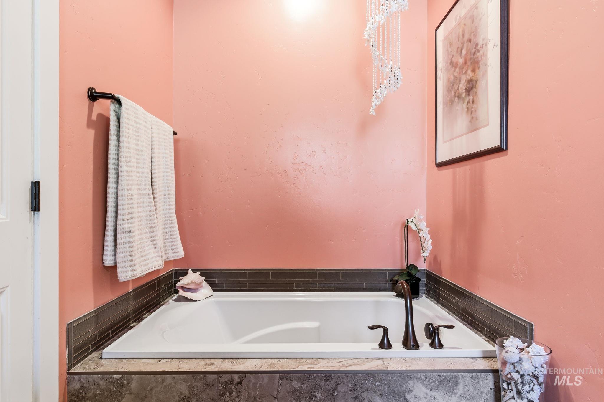 Built-in soaking tub with bronze fixtures, surrounded by a dark stone-look tile deck and a slender accent tile border