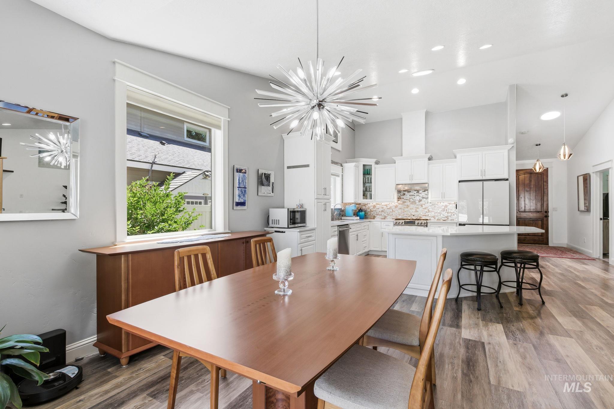 Open-concept kitchen and dining area featuring vaulted ceilings, a contemporary sputnik chandelier, light wood-finish flooring, white cabinetry with a tile backsplash, and a breakfast bar with seating