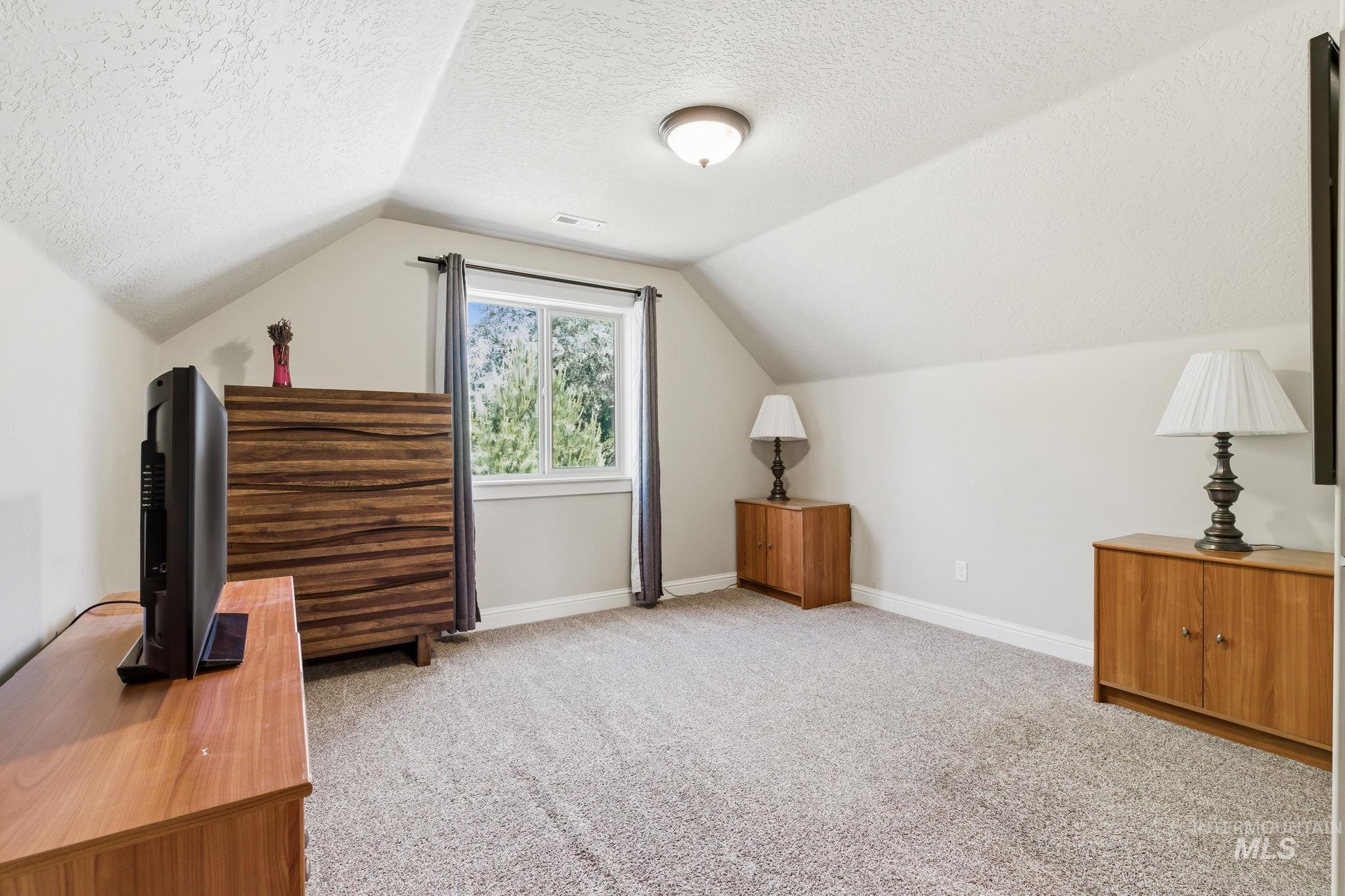 Carpeted room with sloped ceilings and a window featuring natural light
