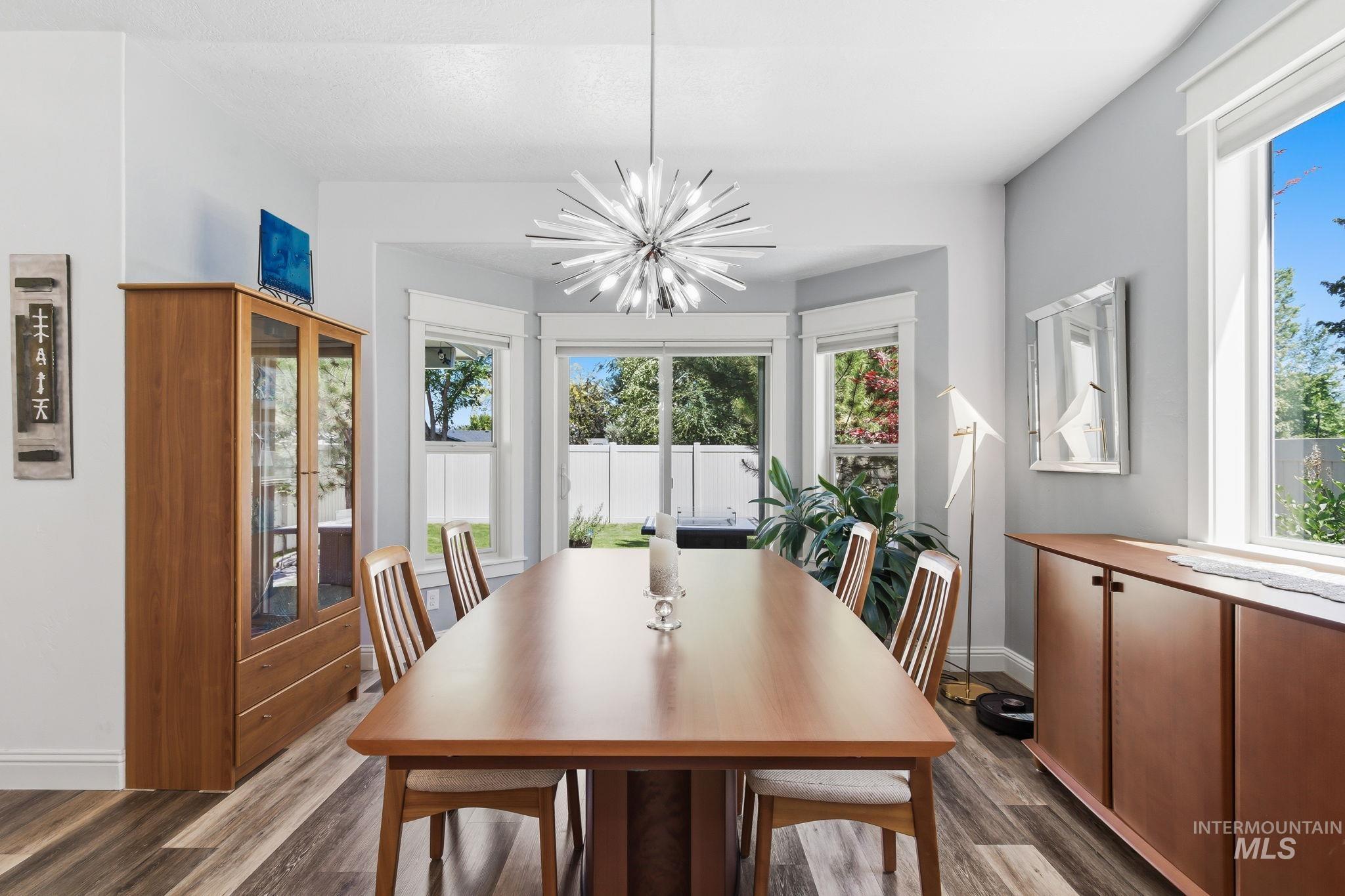 Dining area featuring wood-finish flooring, a modern sputnik chandelier, and a bay window overlooking a fenced yard