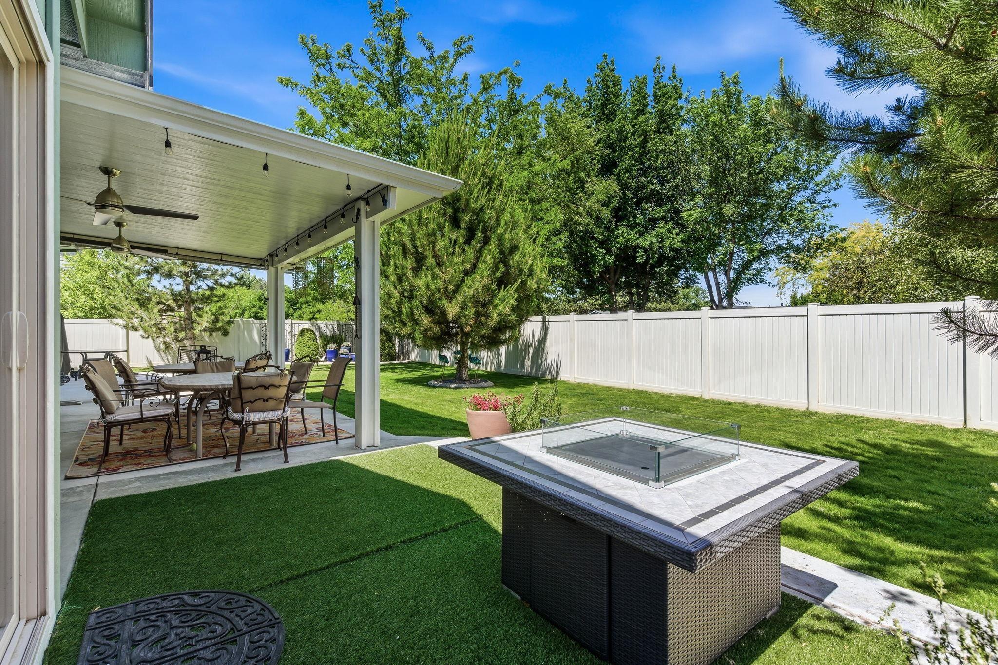 Expansive backyard featuring a covered patio, artificial turf, and a fire pit