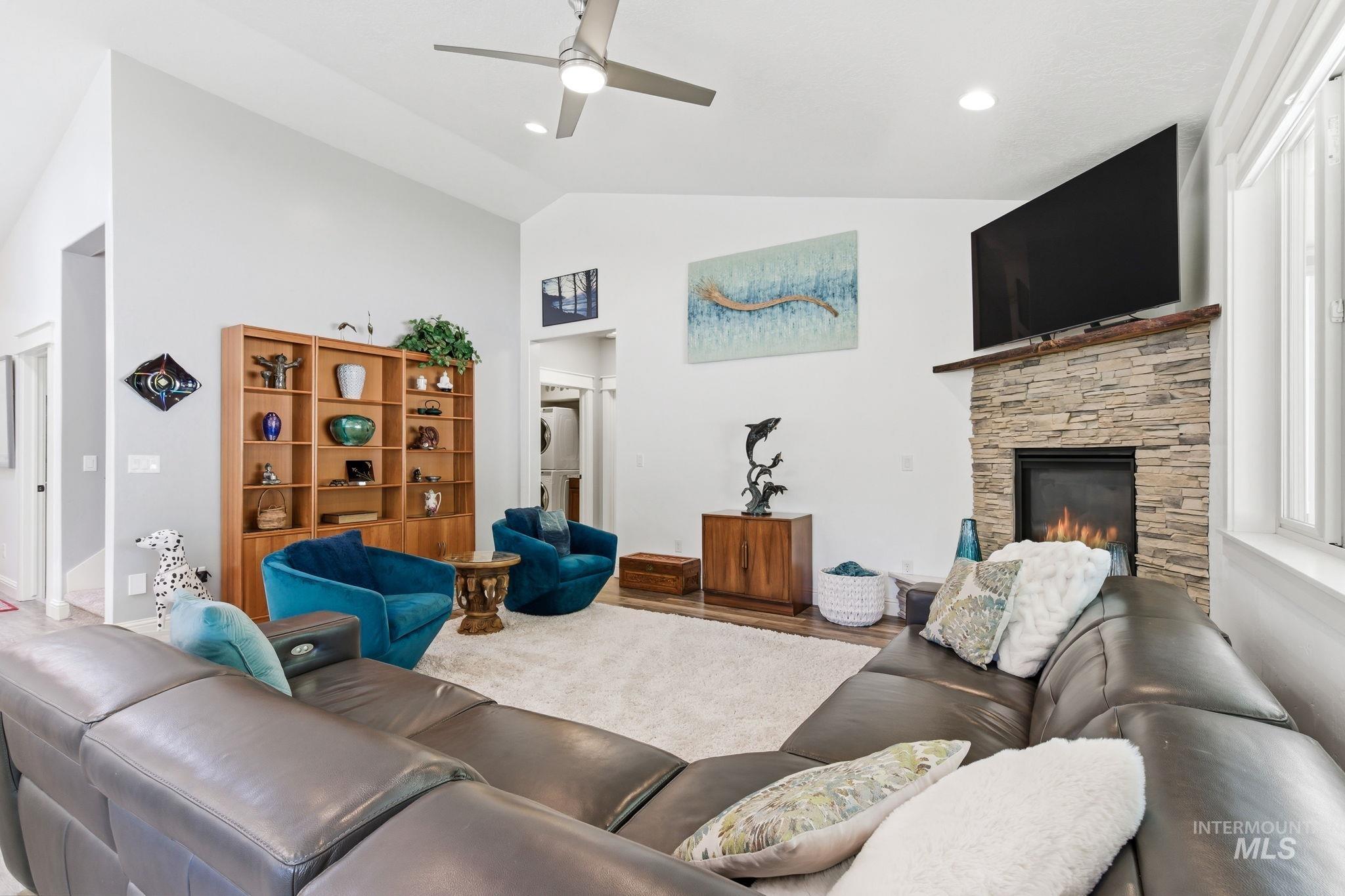 Bright living area featuring vaulted ceilings, a stone fireplace with a wood-finish mantel, recessed lighting, and wood-finish flooring