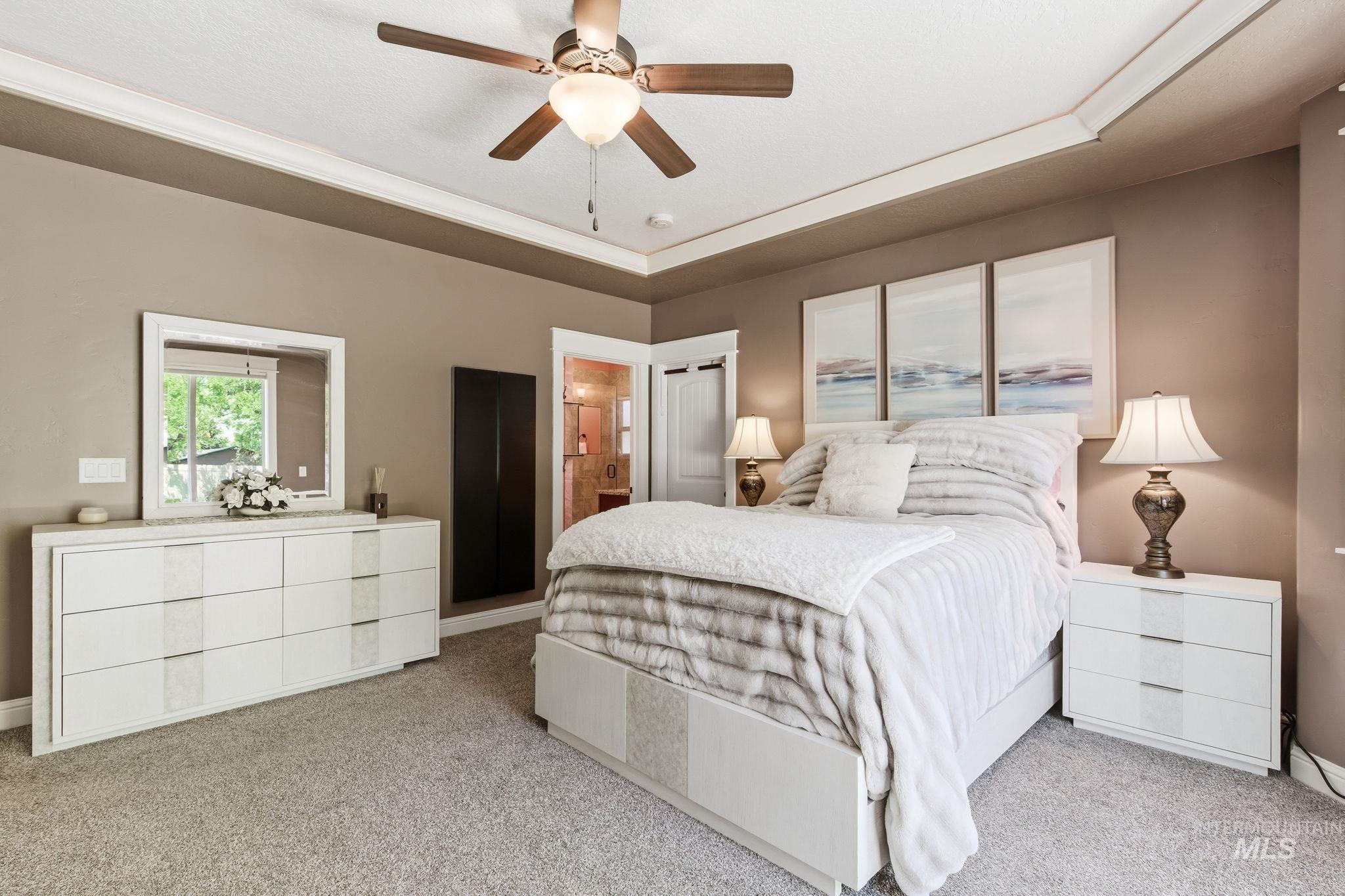 Carpeted bedroom featuring a tray ceiling with crown molding, ceiling fan, and access to a bathroom