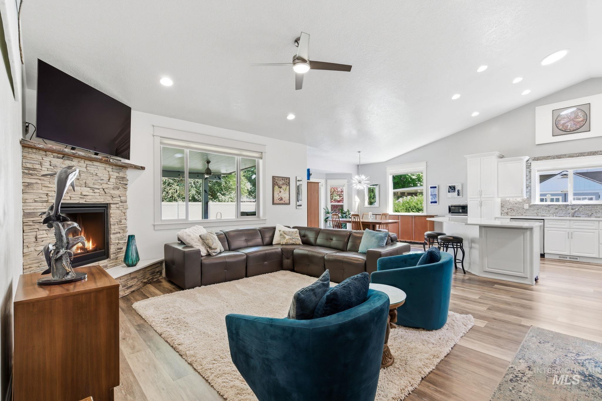 Vaulted ceiling living room featuring a stone-clad fireplace and wood-finish flooring