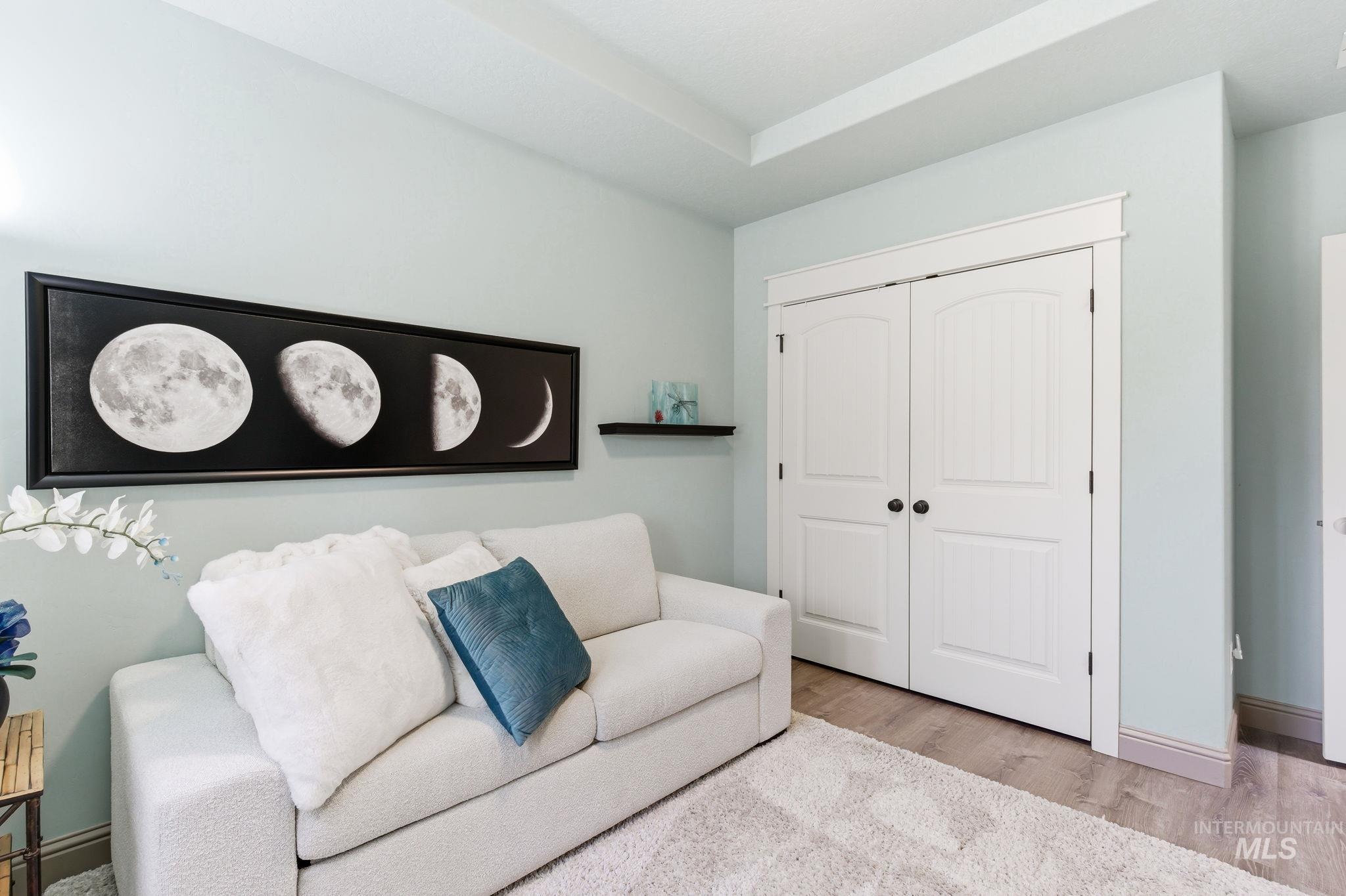 Recessed lighting illuminates a room featuring light-toned walls and wood-finish flooring