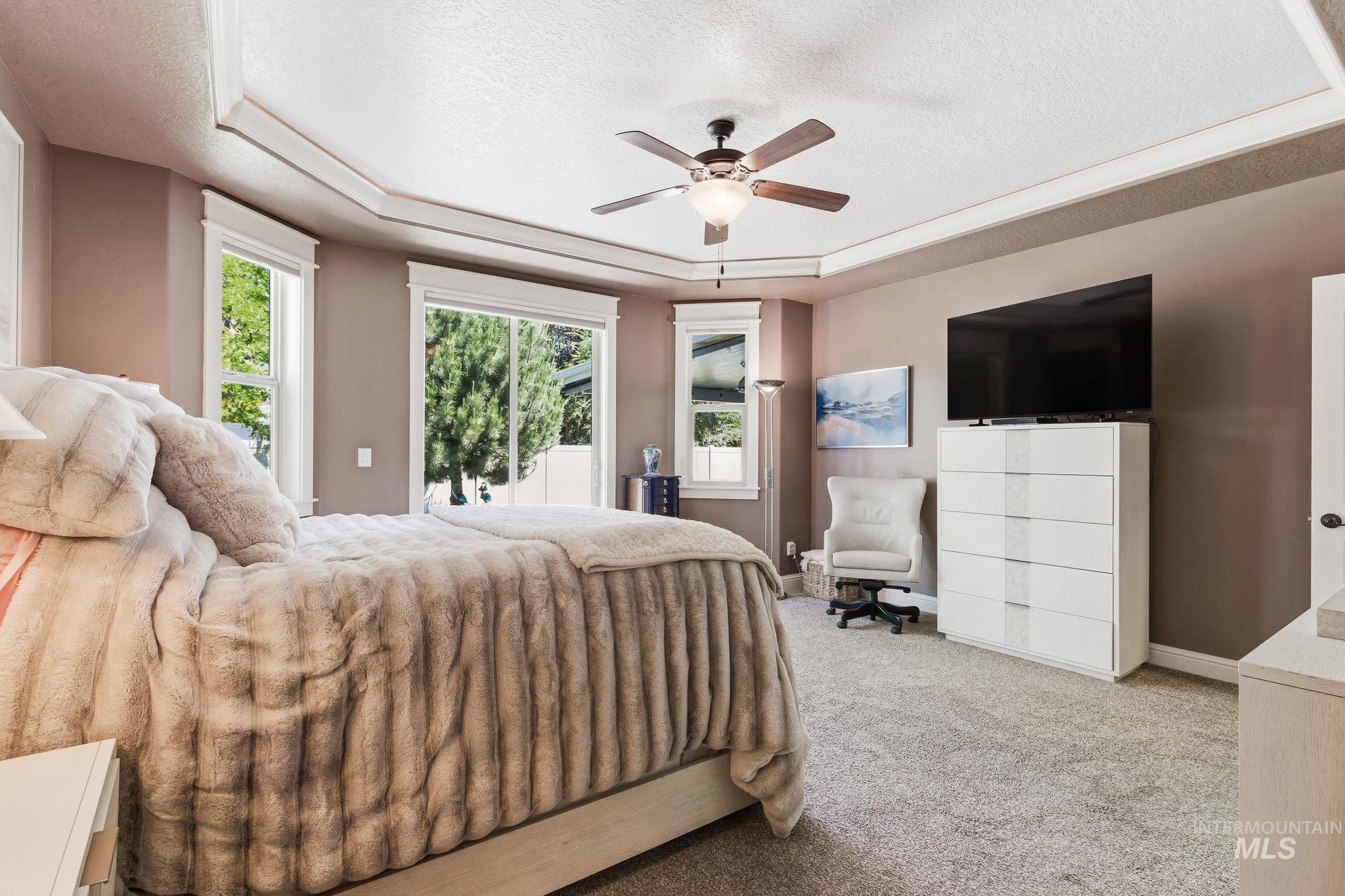 Tray ceiling with recessed lighting and a ceiling fan, carpeted flooring, and multiple windows