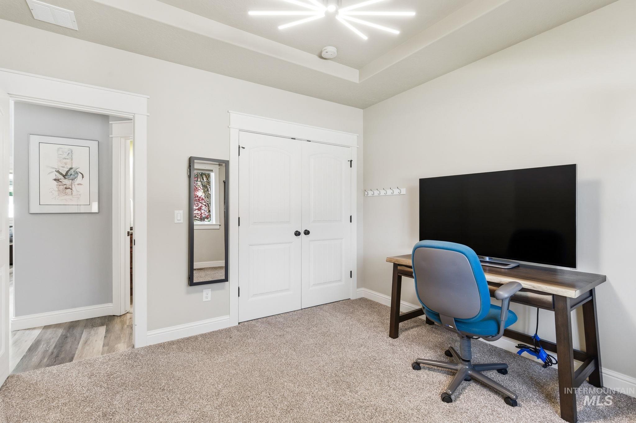 Carpeted room featuring a tray ceiling with a modern light fixture, white bi-fold closet doors, and light-toned walls