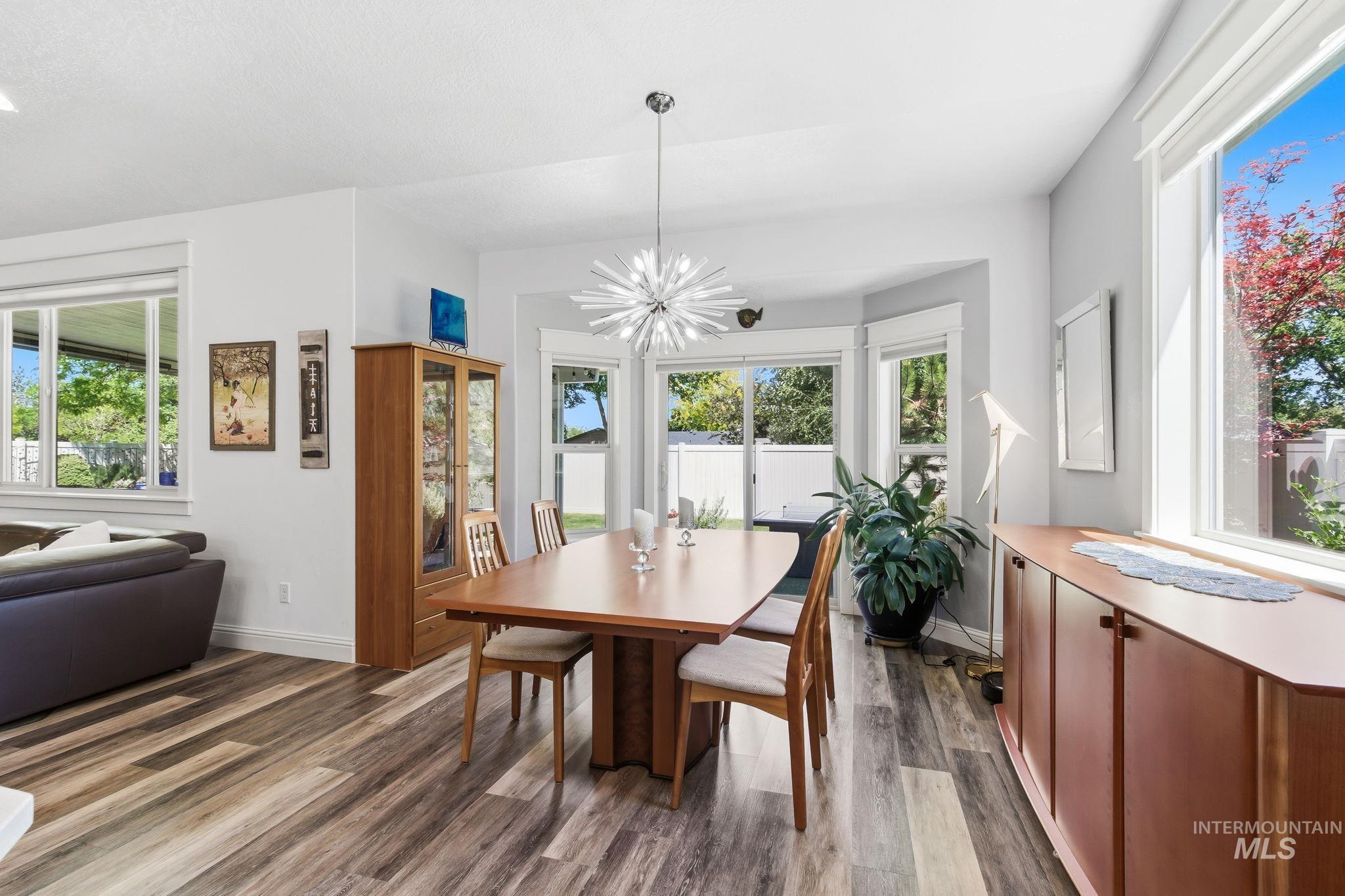 Open-concept dining area featuring wood-finish flooring, a contemporary chandelier, and a bay window with natural light