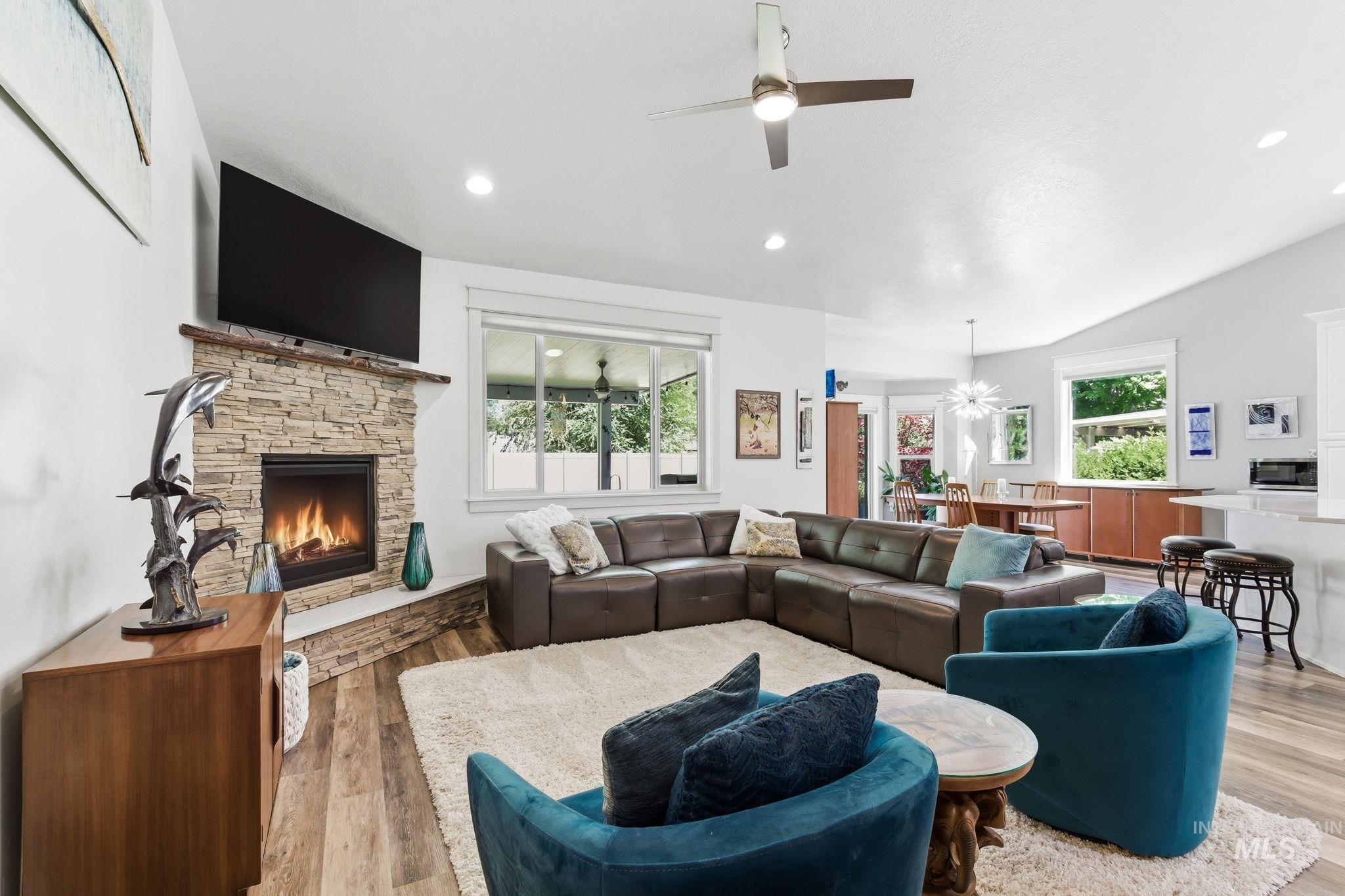 Living space featuring a stone-clad fireplace with a raised hearth, wood-finish flooring, recessed lighting, and a ceiling fan