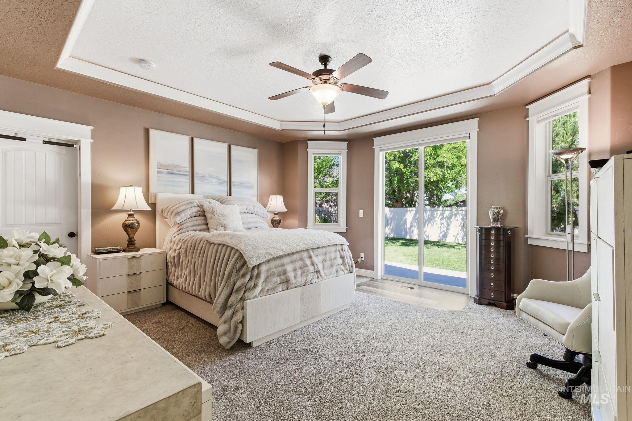 Tray ceiling featuring crown molding and a ceiling fan, with a sliding glass door providing direct outdoor access, accompanied by two additional windows
