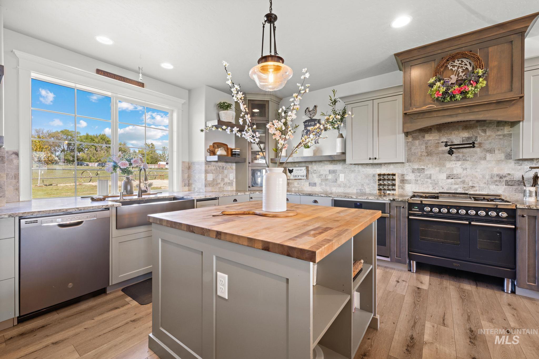 Kitchen with double oven range, open shelves, light stone counters, stainless steel dishwasher, and a center island