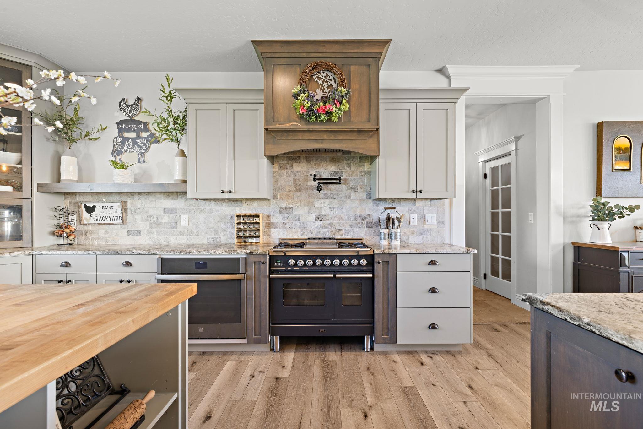 Kitchen featuring light stone counters, range with two ovens, open shelves, and stainless steel oven