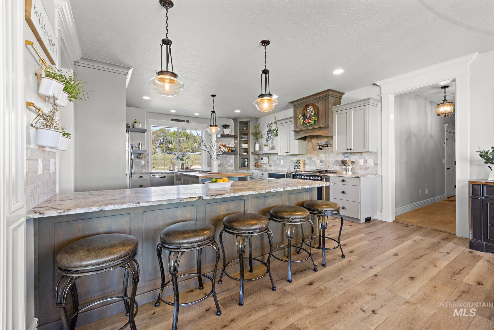 Kitchen with a breakfast bar area, open shelves, light stone counters, decorative light fixtures, and tasteful backsplash
