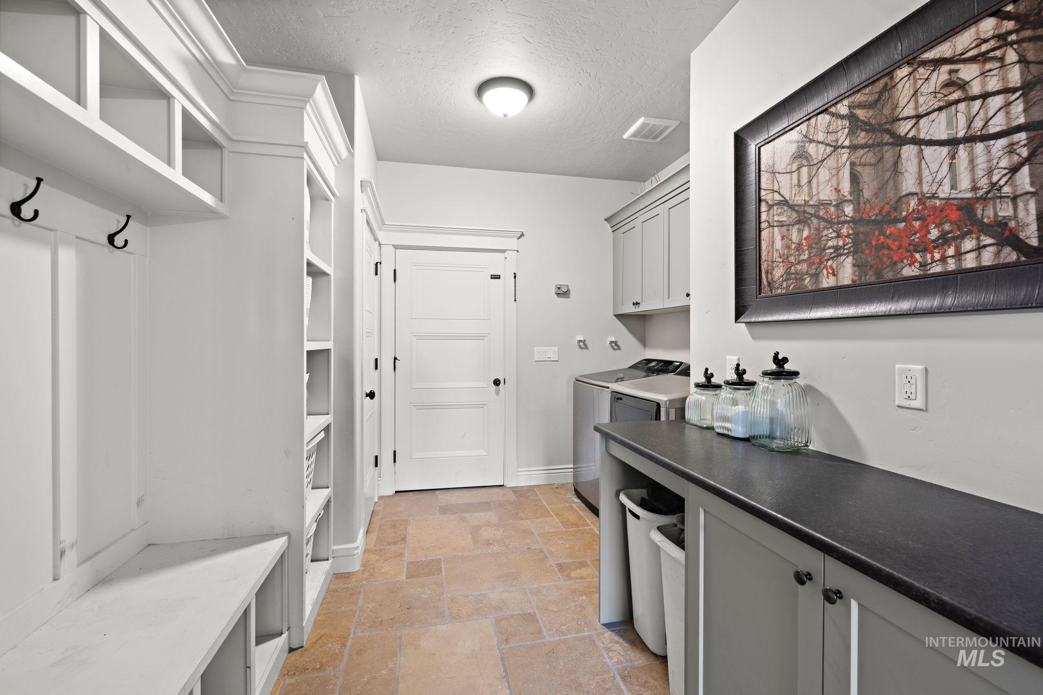 Laundry area with a textured ceiling, stone tile floors, cabinet space, and independent washer and dryer