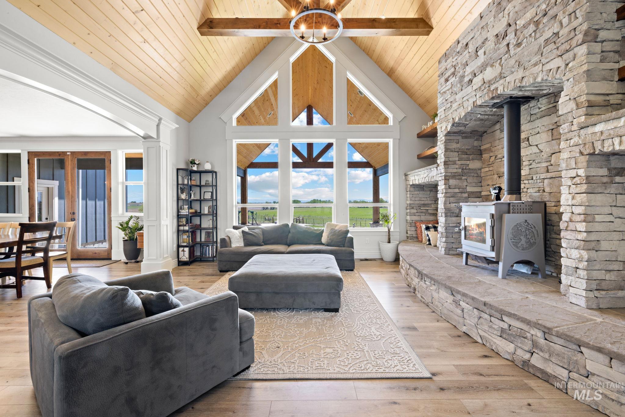 Living area featuring high vaulted ceiling, light wood-type flooring, wooden ceiling, a wood stove, and ornate columns
