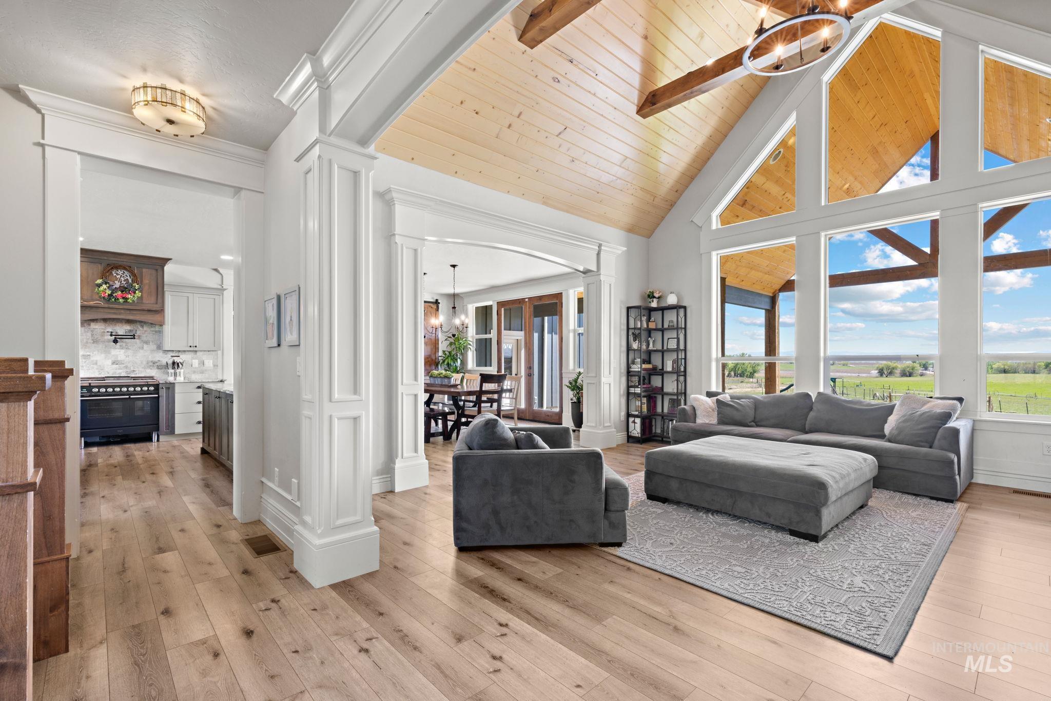 Living area featuring a chandelier, decorative columns, high vaulted ceiling, light wood-style flooring, and a wooden ceiling with exposed beams