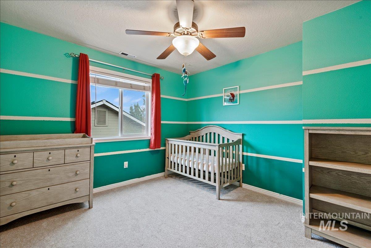 Bedroom with light colored carpet, a crib, a ceiling fan, and a textured ceiling