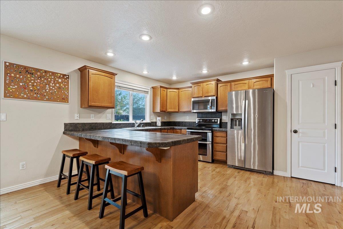 Kitchen with appliances with stainless steel finishes, a kitchen breakfast bar, recessed lighting, light wood-style floors, and a peninsula