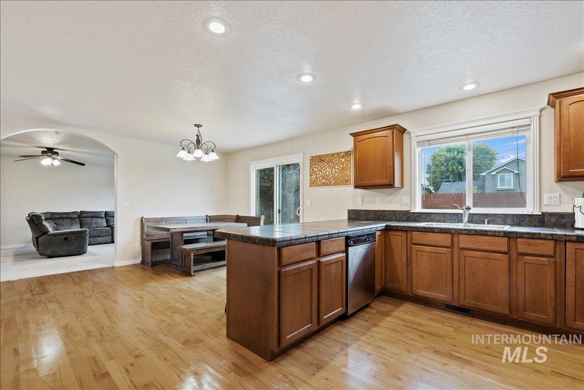 Kitchen with a textured ceiling, brown cabinetry, a peninsula, light wood finished floors, and decorative light fixtures